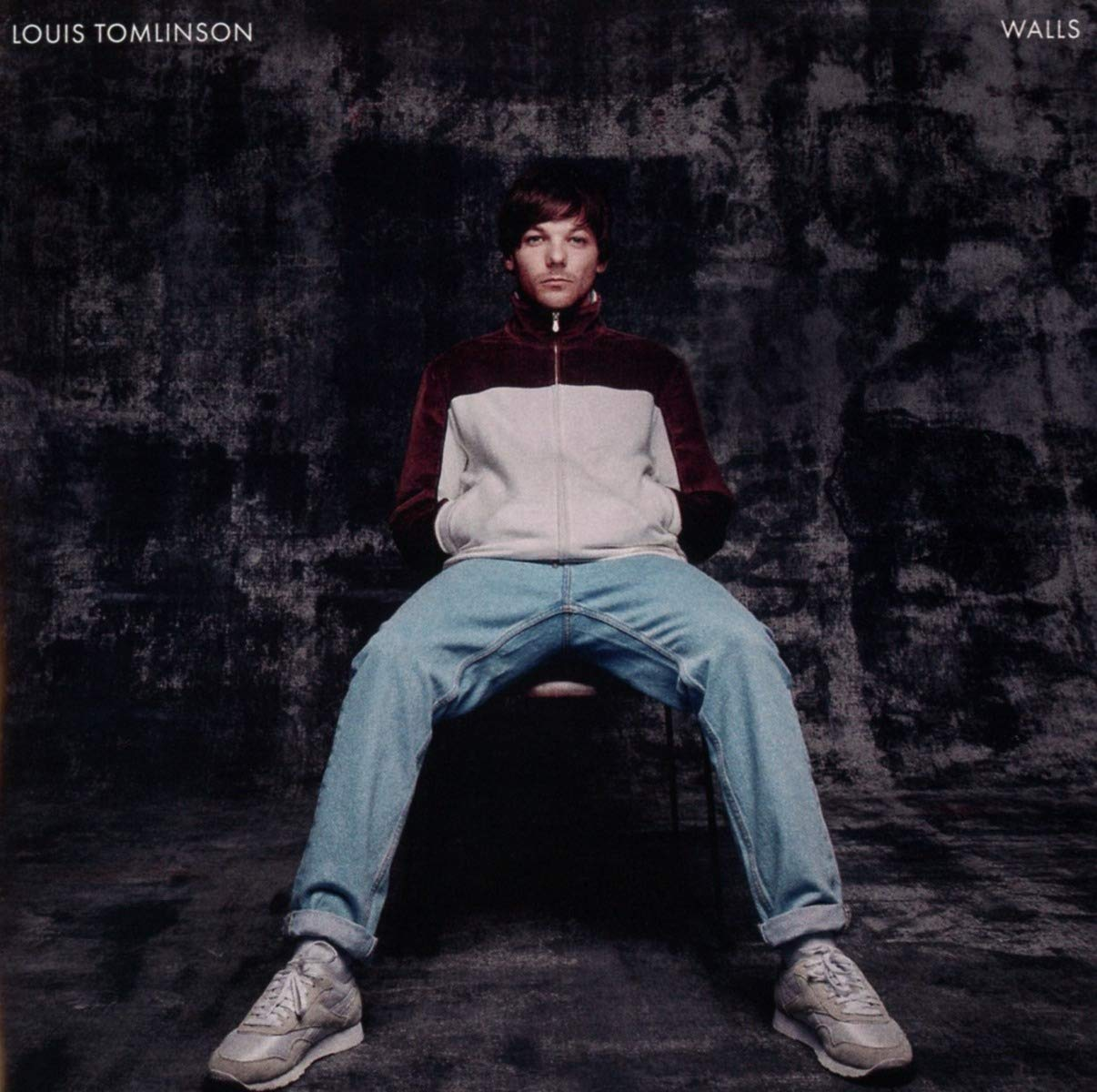Louis Tomlinson, széken ül, dzsekit és farmert visel.