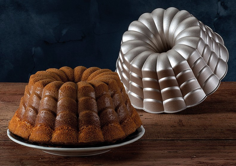 Ein Kuchen und eine Backform. Der Kuchen ist braun und auf einem Teller, die Form ist silber.