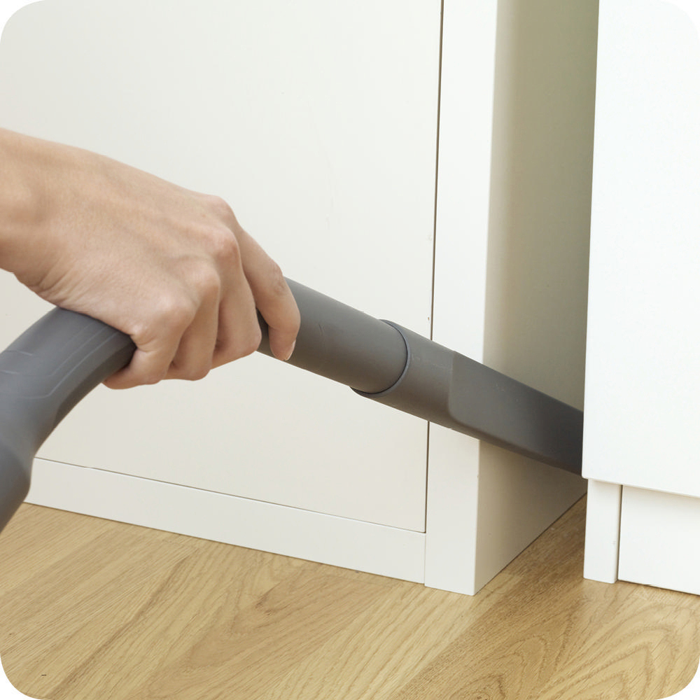 Eine Hand, die einen Staubsauger benutzt, um einen Raum zwischen weißen Schränken zu reinigen.