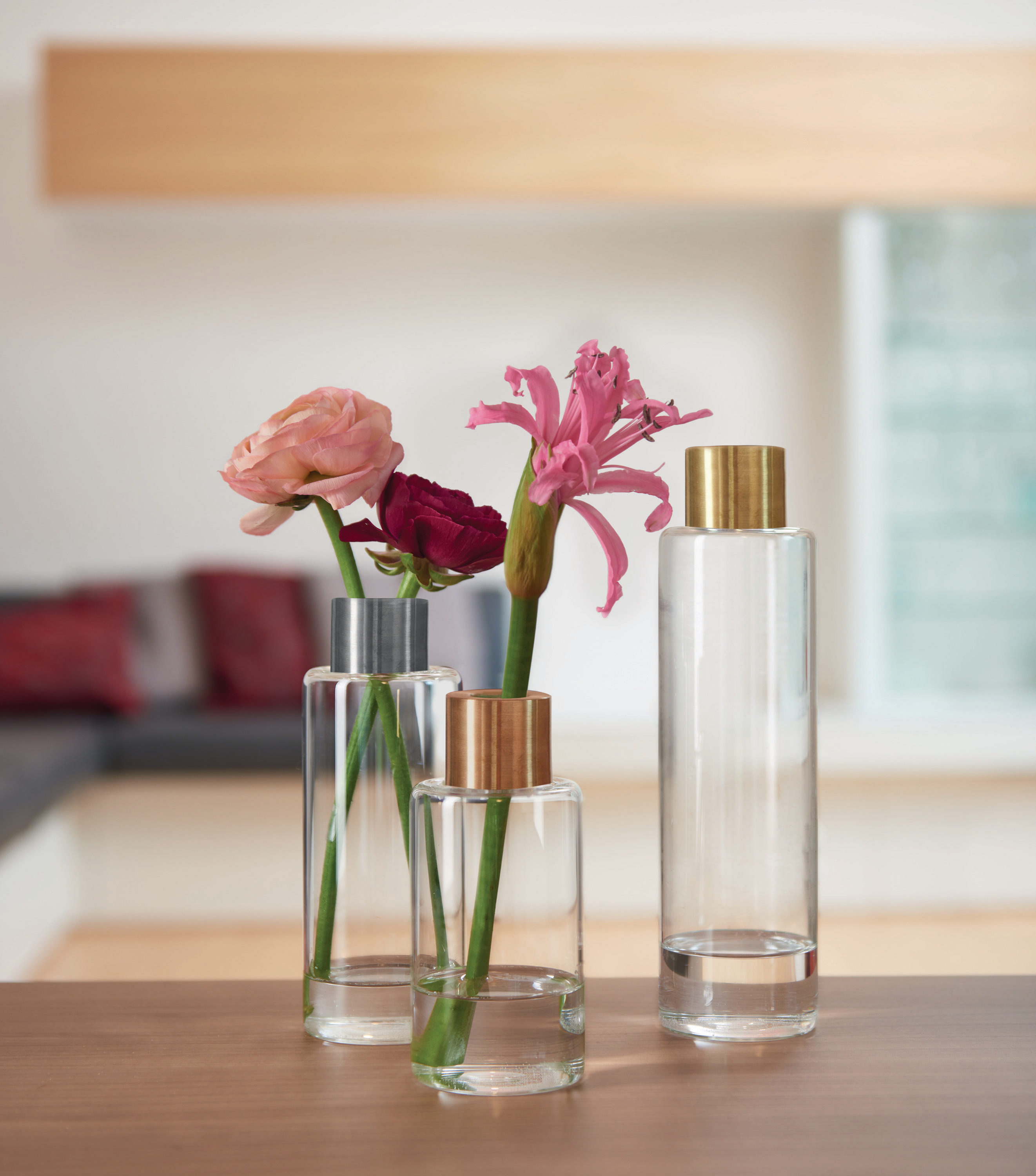 Drei Vasen mit Blumen auf einem Tisch, vor verschwommenem Hintergrund.