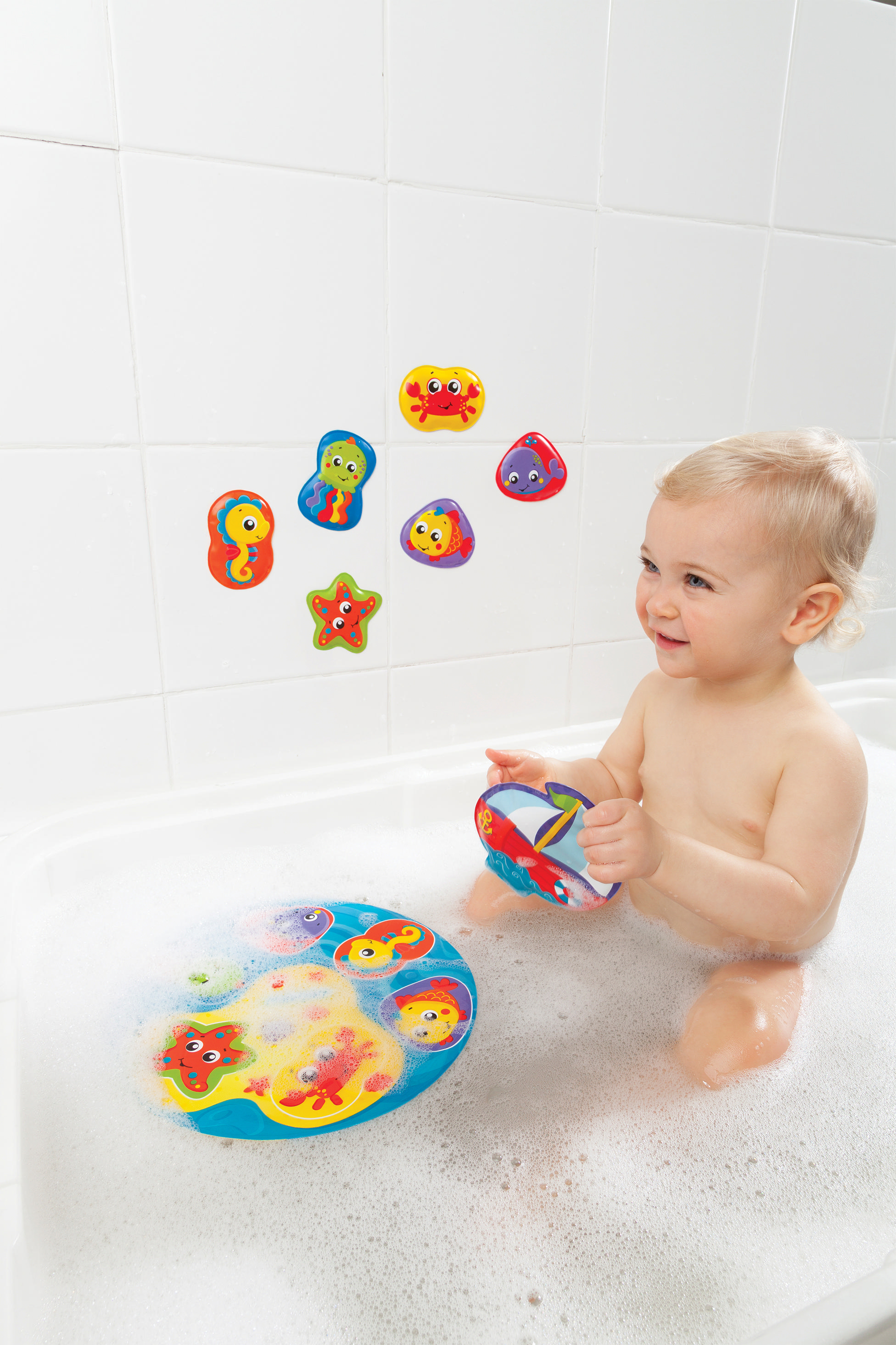 Ein Baby sitzt in einer Wanne mit Blasen. An der Wand sind Aufkleber.