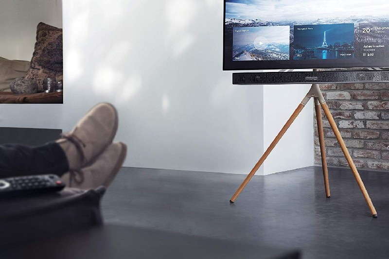 Un televisor en un soporte de madera. Una persona se relaja en el sofá con los pies en alto.