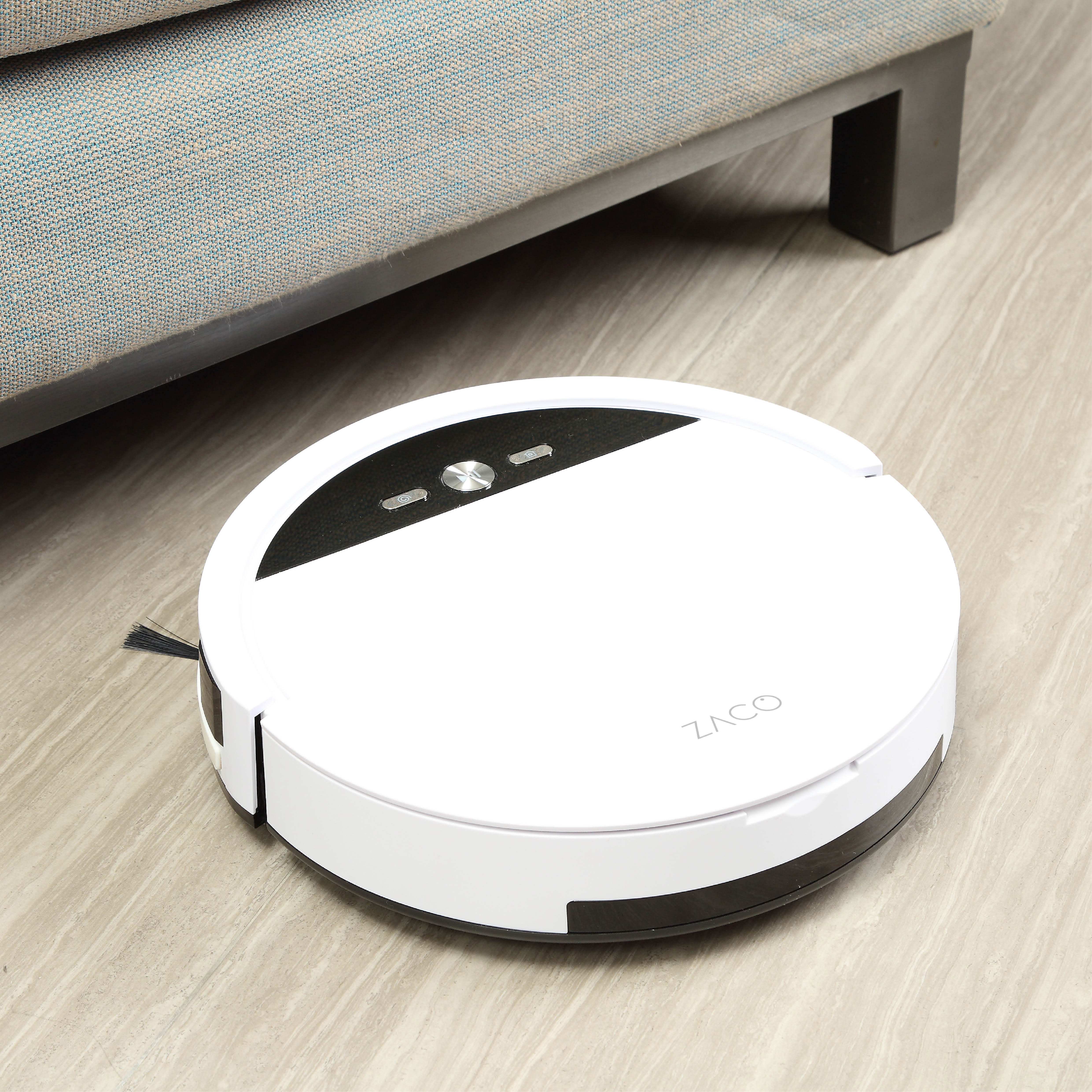 Weißer Roboter-Staubsauger auf hellem Holzboden neben einer grauen Couch.