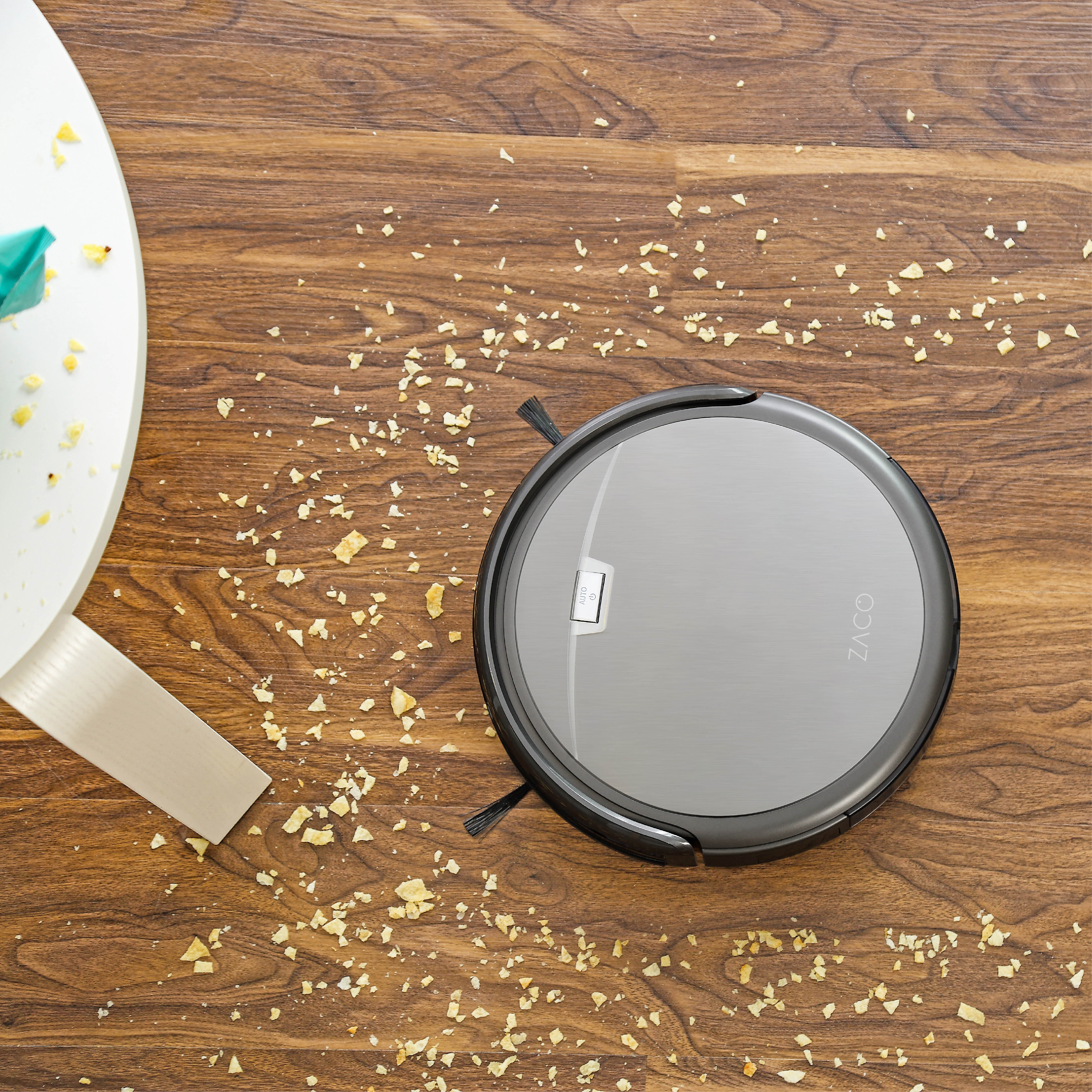 Ein Roboter-Staubsauger auf einem Holzboden mit Rückständen von einem hellen Objekt.
