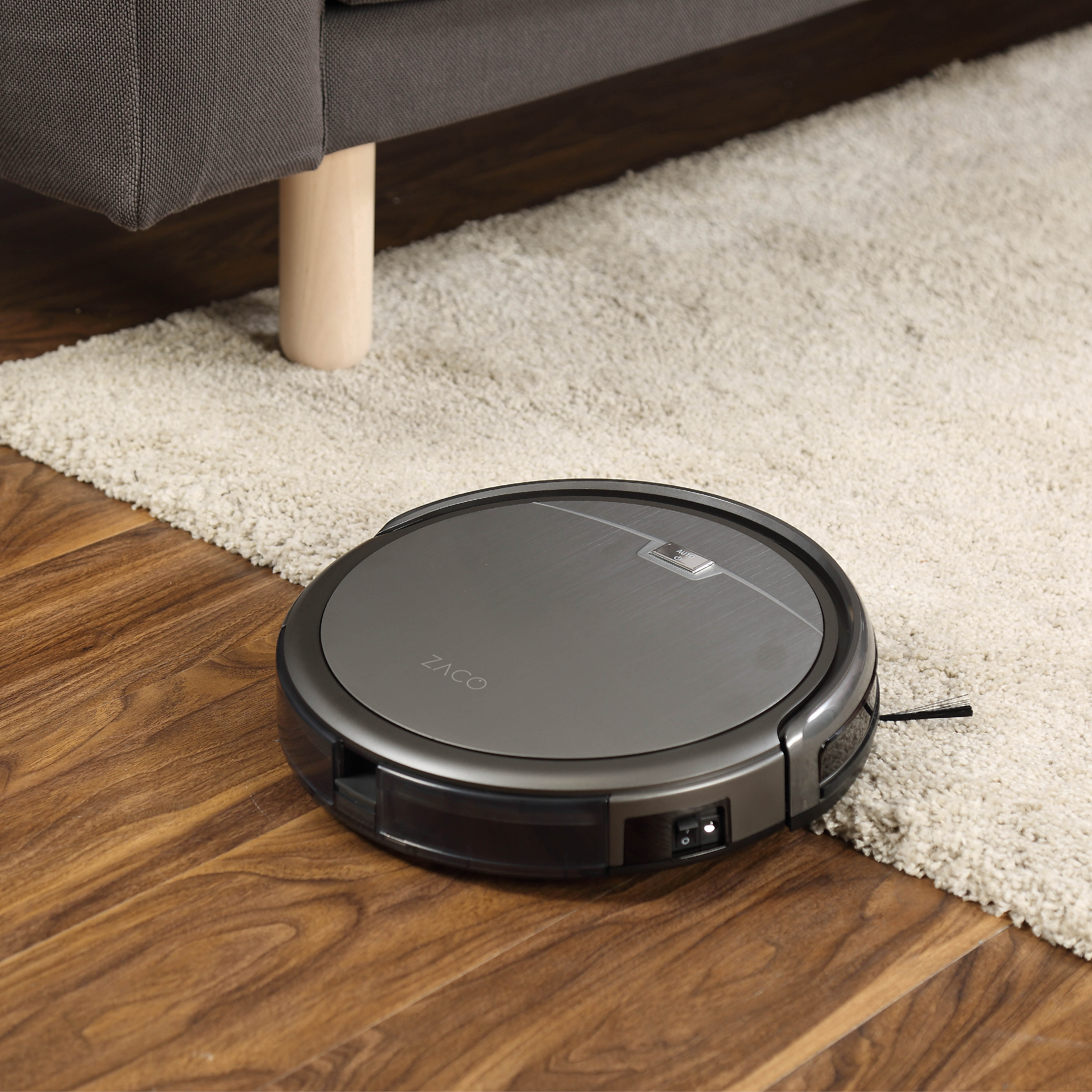 Ein Roboter-Staubsauger reinigt einen Holzboden neben einem Teppich.