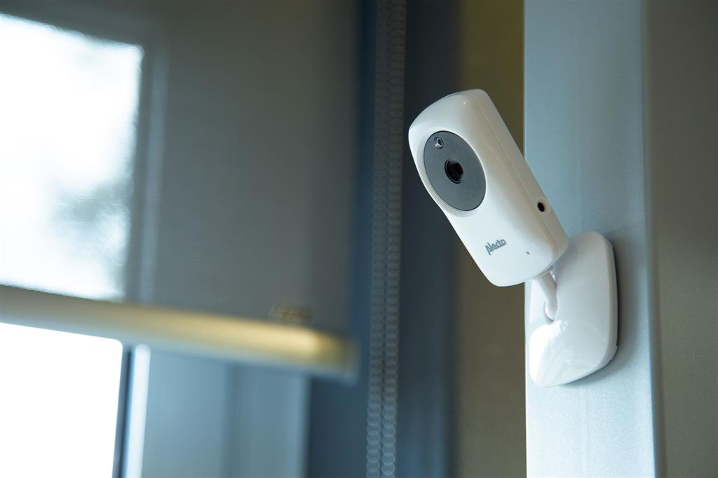 Un moniteur pour bébé blanc sur un mur gris. Une fenêtre avec des stores en arrière-plan.