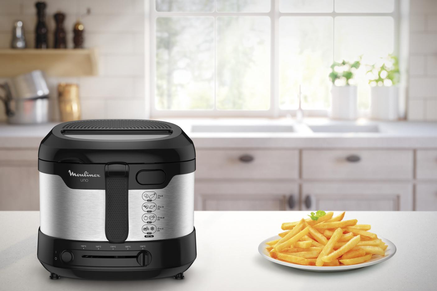 Une friteuse Moulinex Uno noire et argentée avec des frites dans une assiette dans une cuisine.