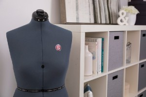 Schneiderpuppe in einem Raum mit Regalen, Büchern und Nähutensilien.