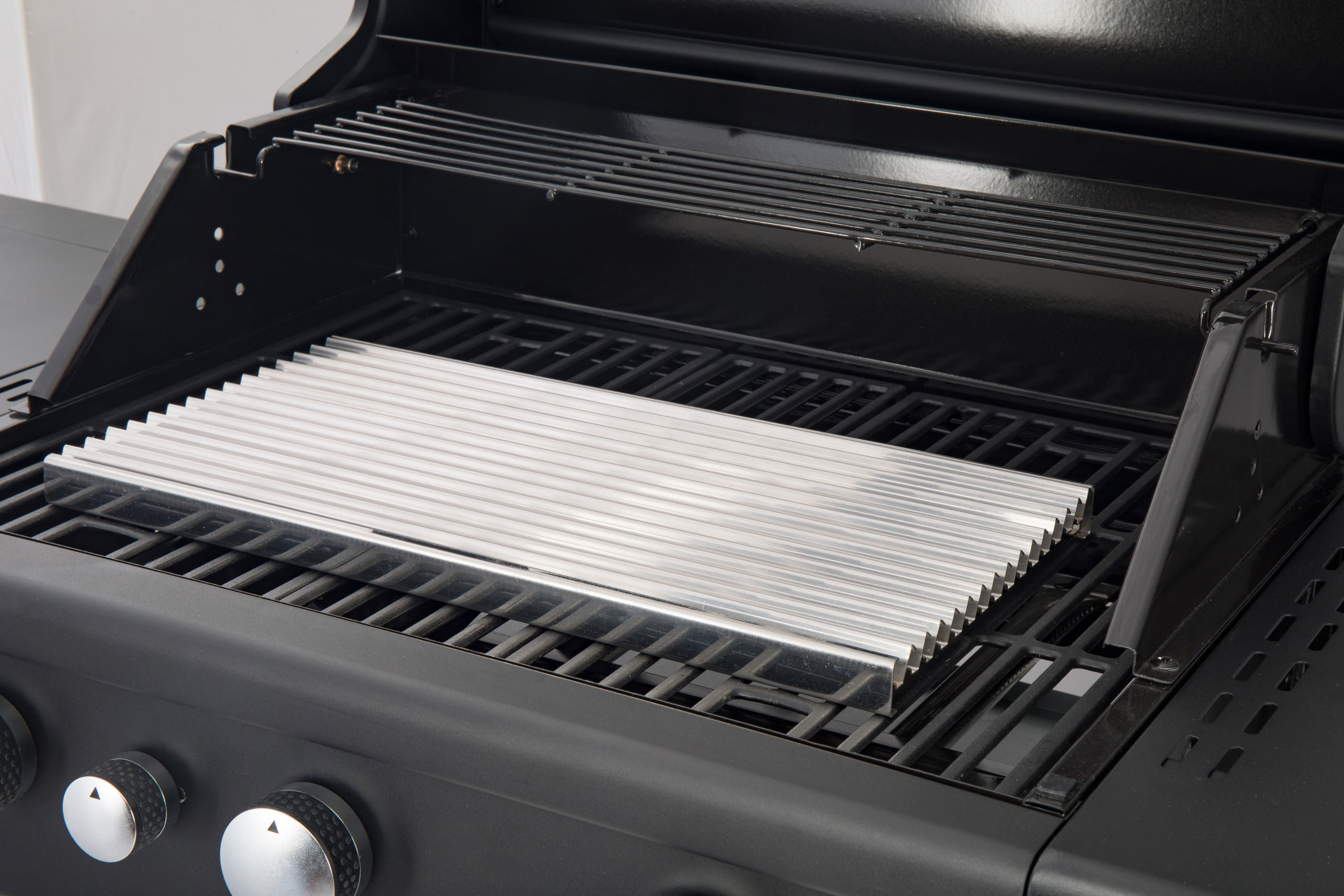 Schwarzer Grill mit Metallrost im Inneren. Der Grill ist geöffnet. Der Hintergrund ist unscharf.