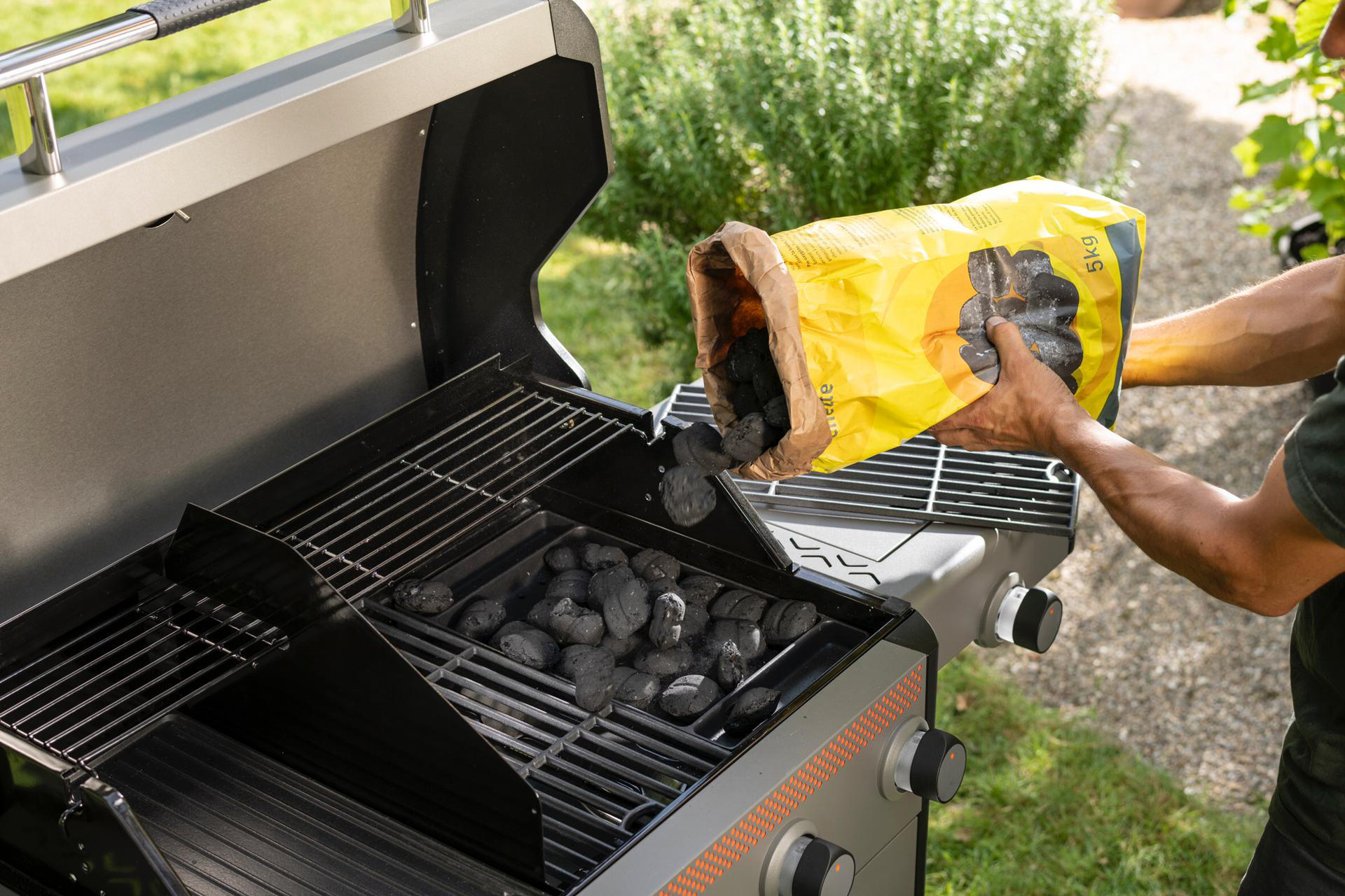 Eine Person gießt Holzkohle aus einem gelben Beutel in einen Grill.