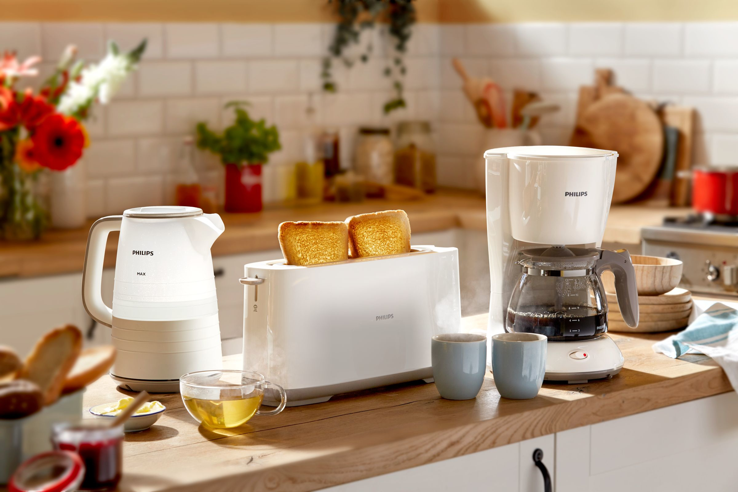 Kitchen with kettle, toaster, coffee machine, cups, and bread on a wooden countertop.