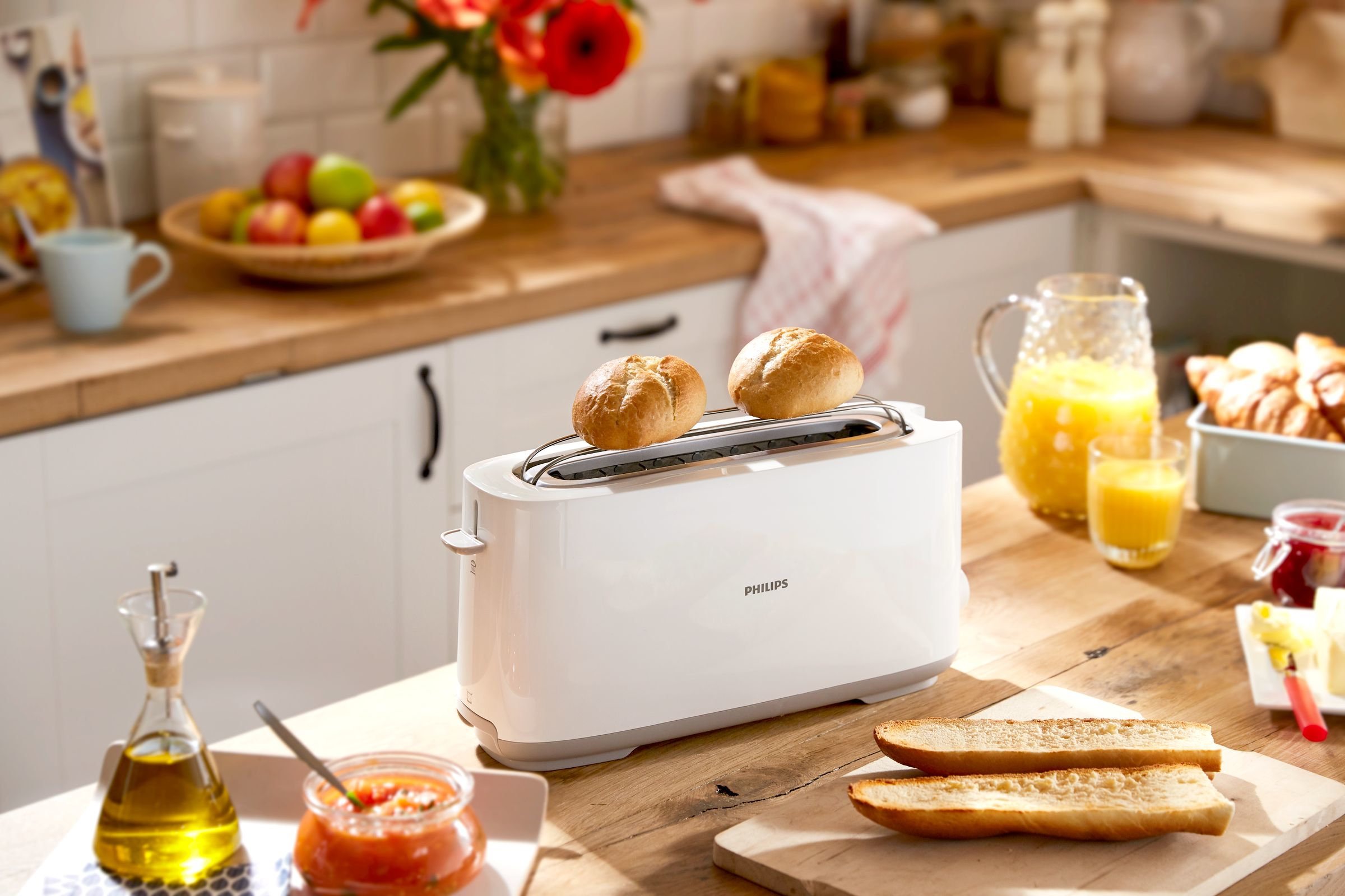 White toaster with two toasted buns on top. Other breakfast items are on the table.