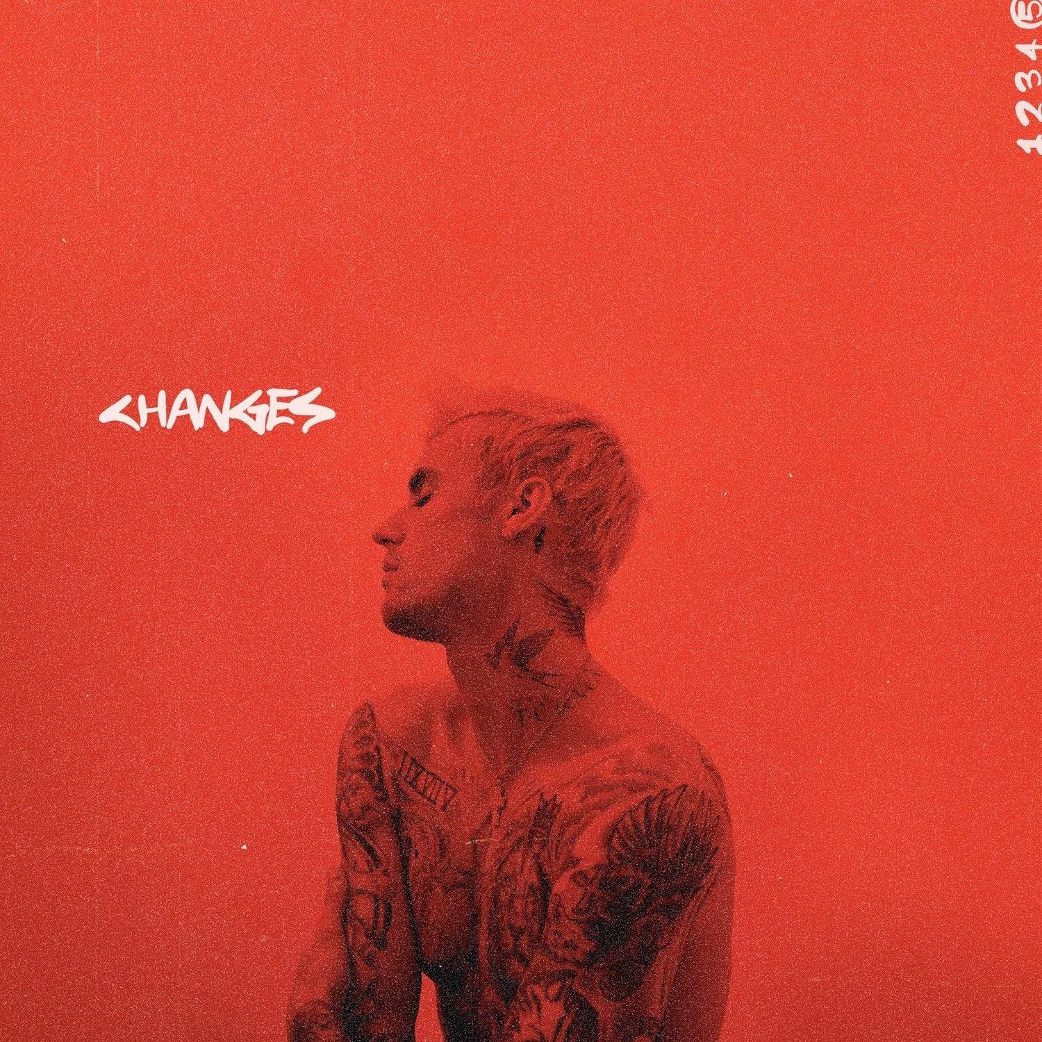 Albumhoes: Justin Bieber, ontbloot bovenlijf met tatoeages, kijkt links op rode achtergrond.