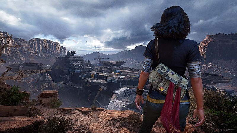 Mujer mirando una base futurista en un cañón. Lleva una mochila con una bufanda roja.