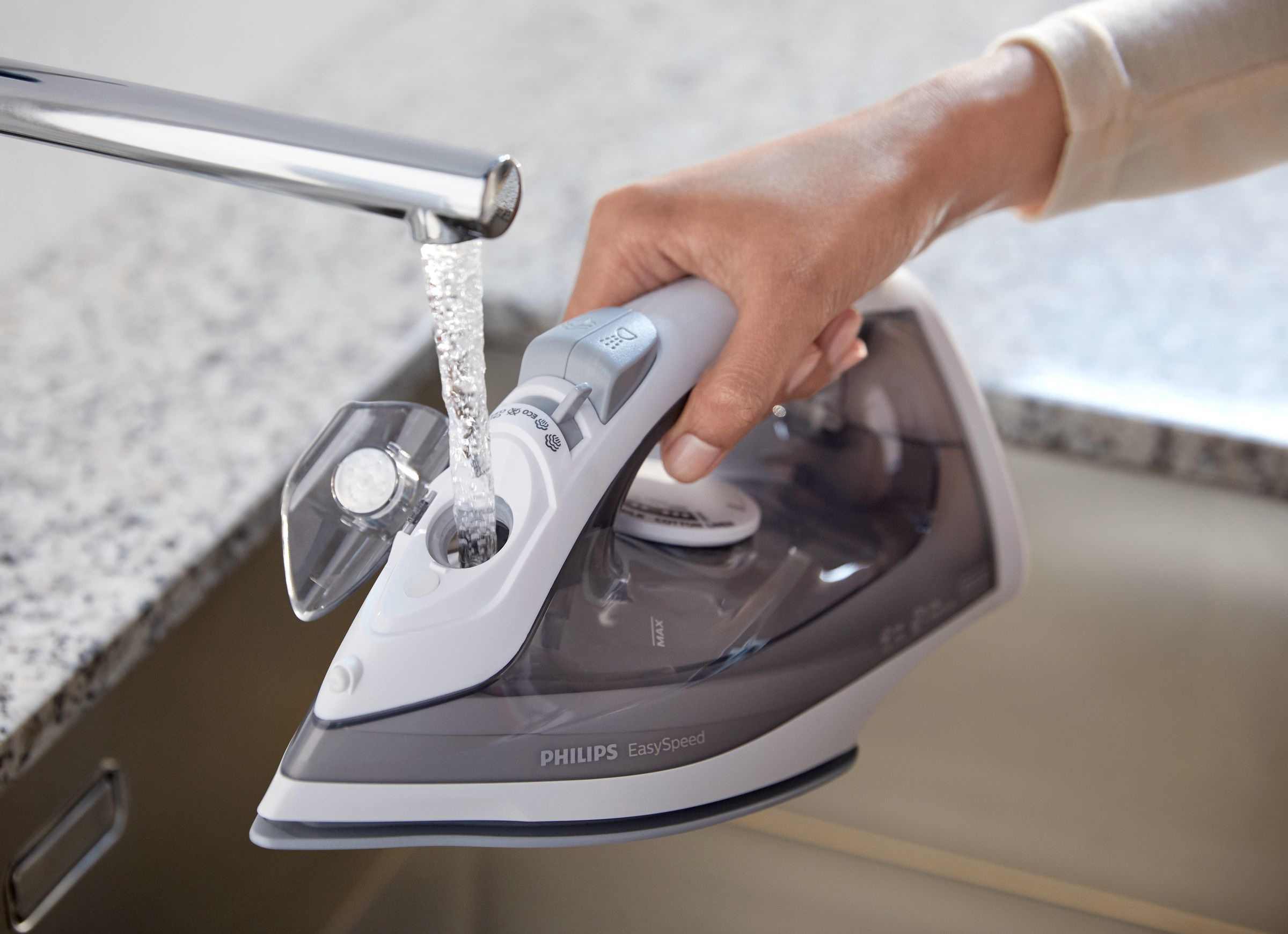 Hand gießt Wasser in ein weißes und graues Philips Bügeleisen über einem Waschbecken. Wasser füllt das Eisen.