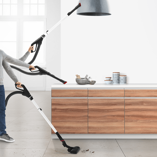 Staubsauger in Gebrauch. Person saugt Boden und Decke. Küche und weiße Wand im Hintergrund.