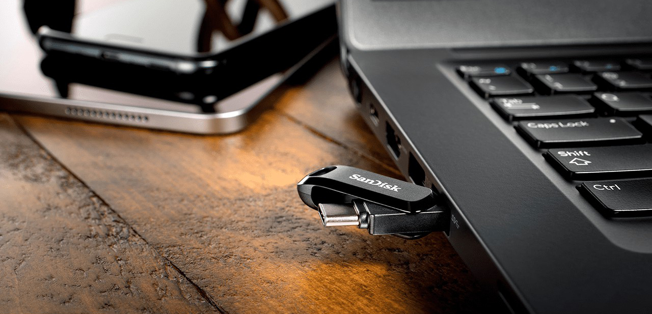 A SanDisk USB-C flash drive plugged into a laptop, with a phone nearby.