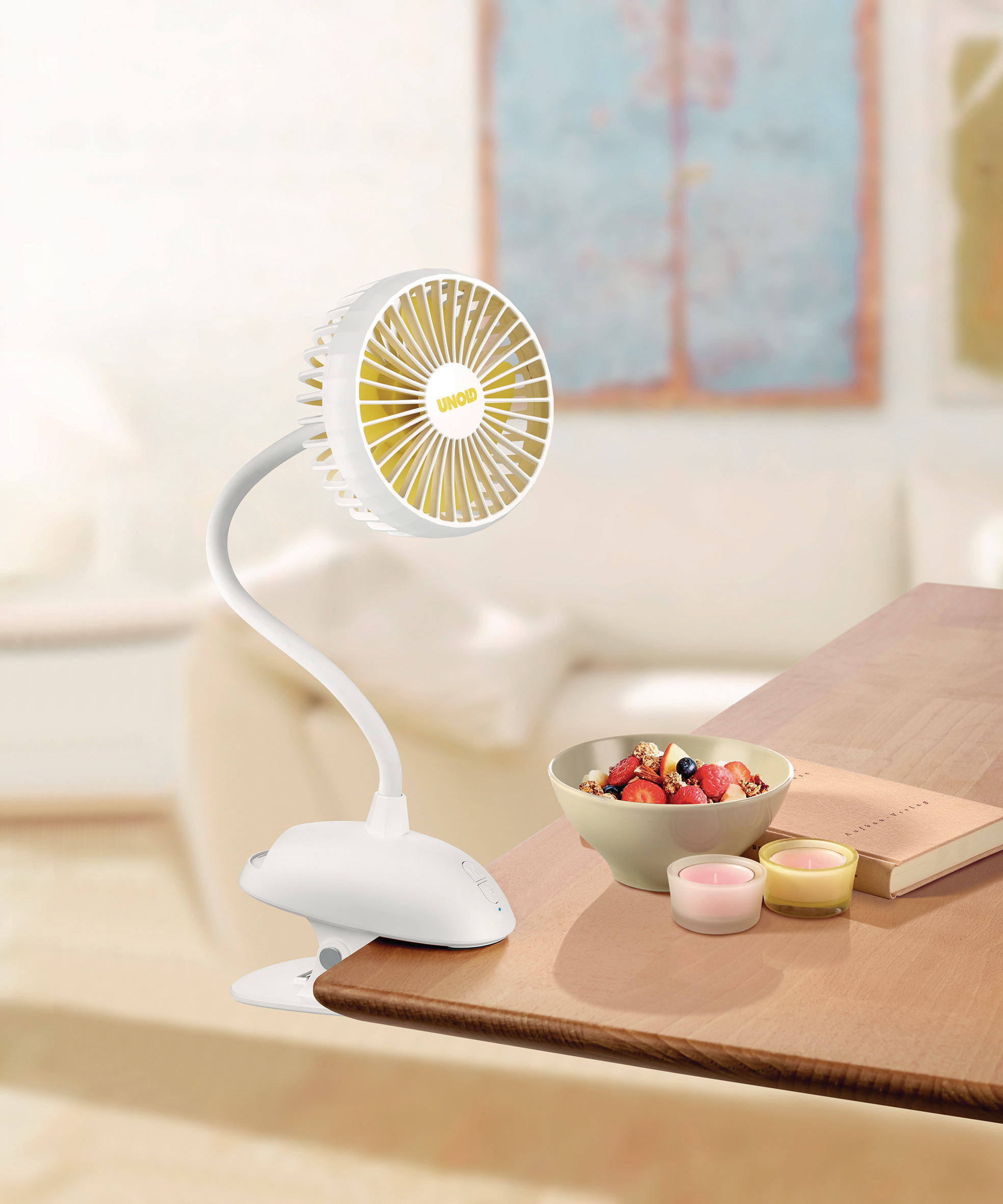 Weißer Ventilator auf einem Schreibtisch. Obstschale und Kerzen sind auch auf dem Tisch.