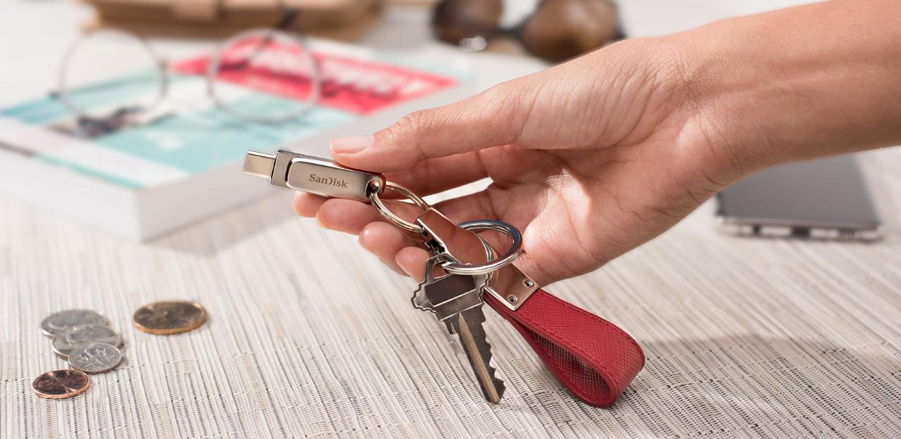 Main tenant une clé USB attachée à des clés et une lanière rouge.