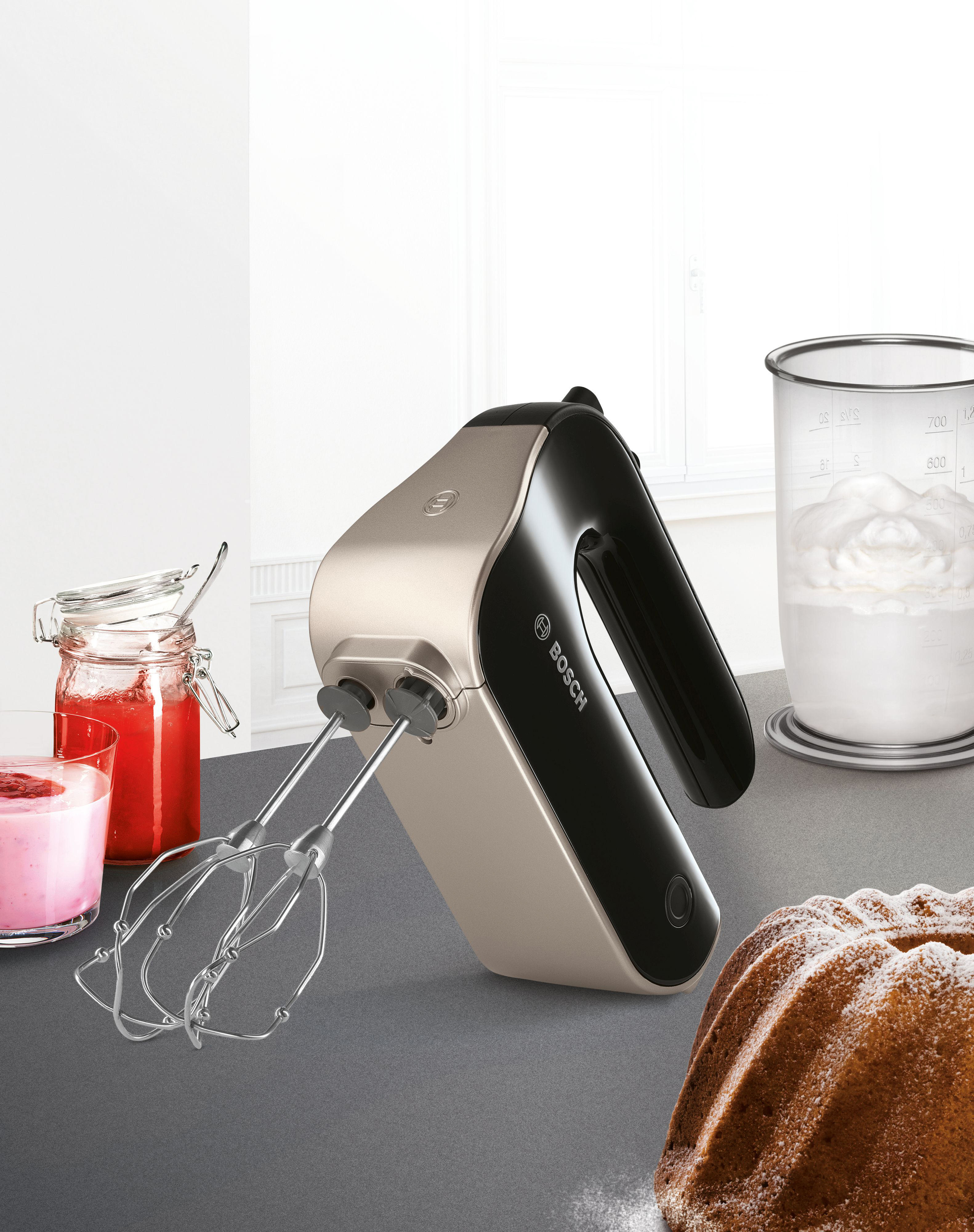 Ein cremefarbener und schwarzer Handmixer mit Aufsätzen und Kuchen.