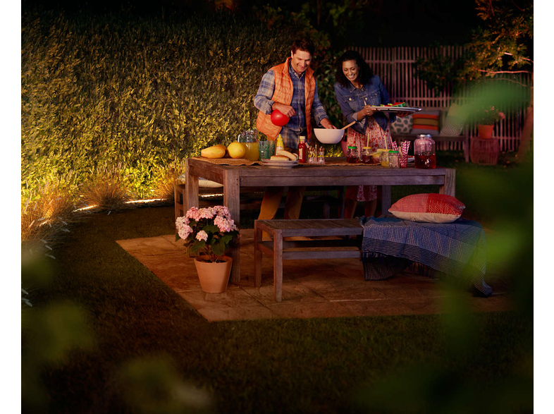 Un couple prépare un dîner en plein air, éclairé par une lumière chaude.
