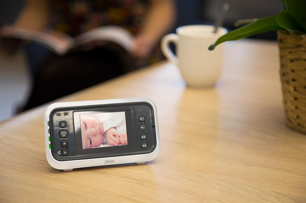 Babyphone auf Holztisch, Person im Hintergrund.