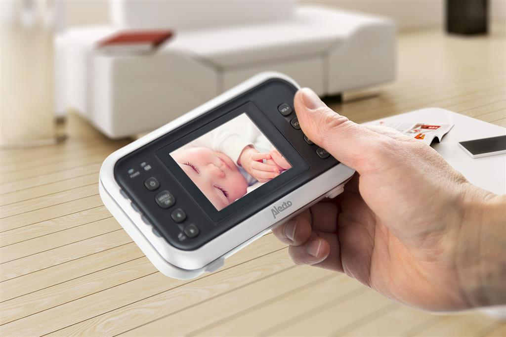 Ein Babyphone mit Bildschirm zeigt ein schlafendes Baby, Nahaufnahme der Hand.
