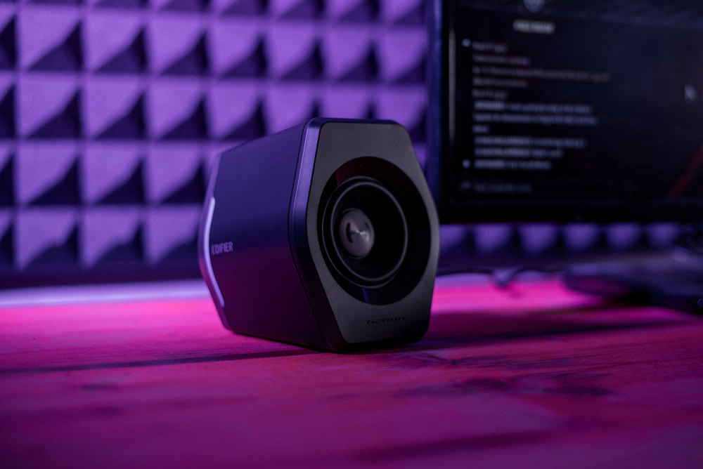 Schwarzer Edifier-Lautsprecher auf einem Holztisch mit lila Hintergrund.