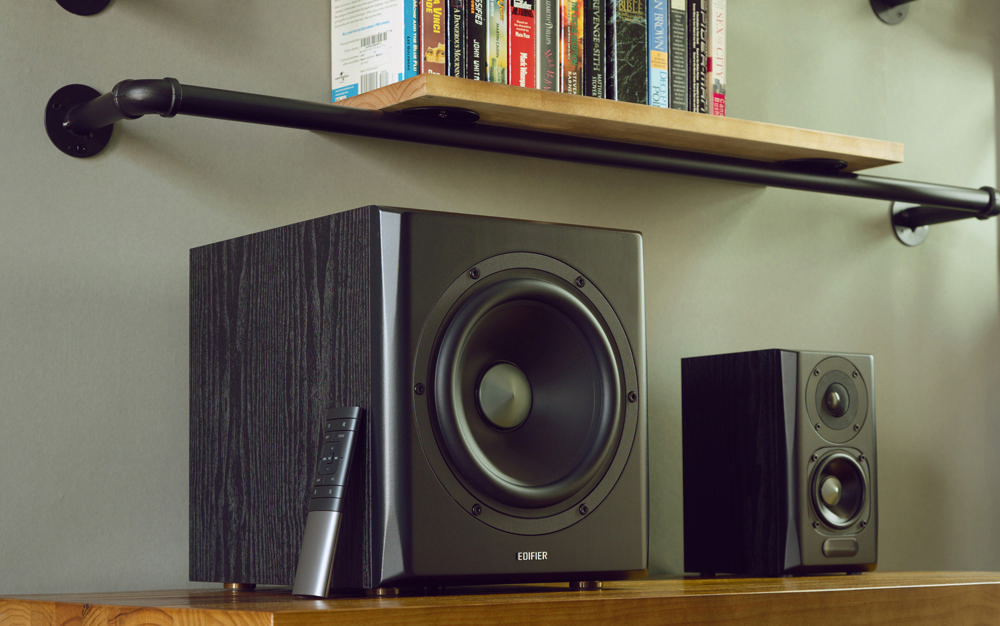 Ein Subwoofer und zwei Lautsprecher auf einem Regal, mit einer Fernbedienung.