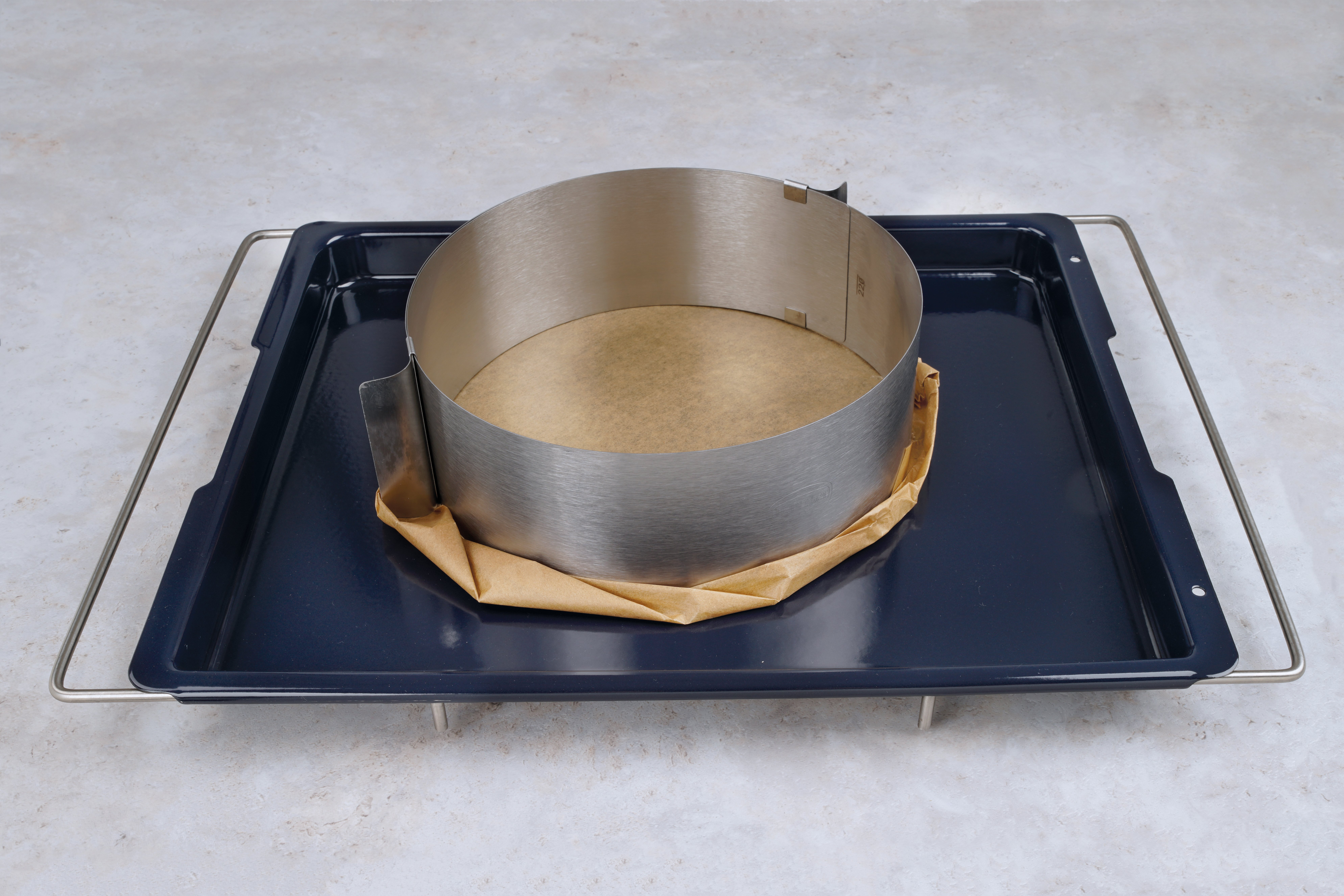 Backblech mit Backpapier und einem Metallring für einen Kuchenboden, bereit zum Backen.
