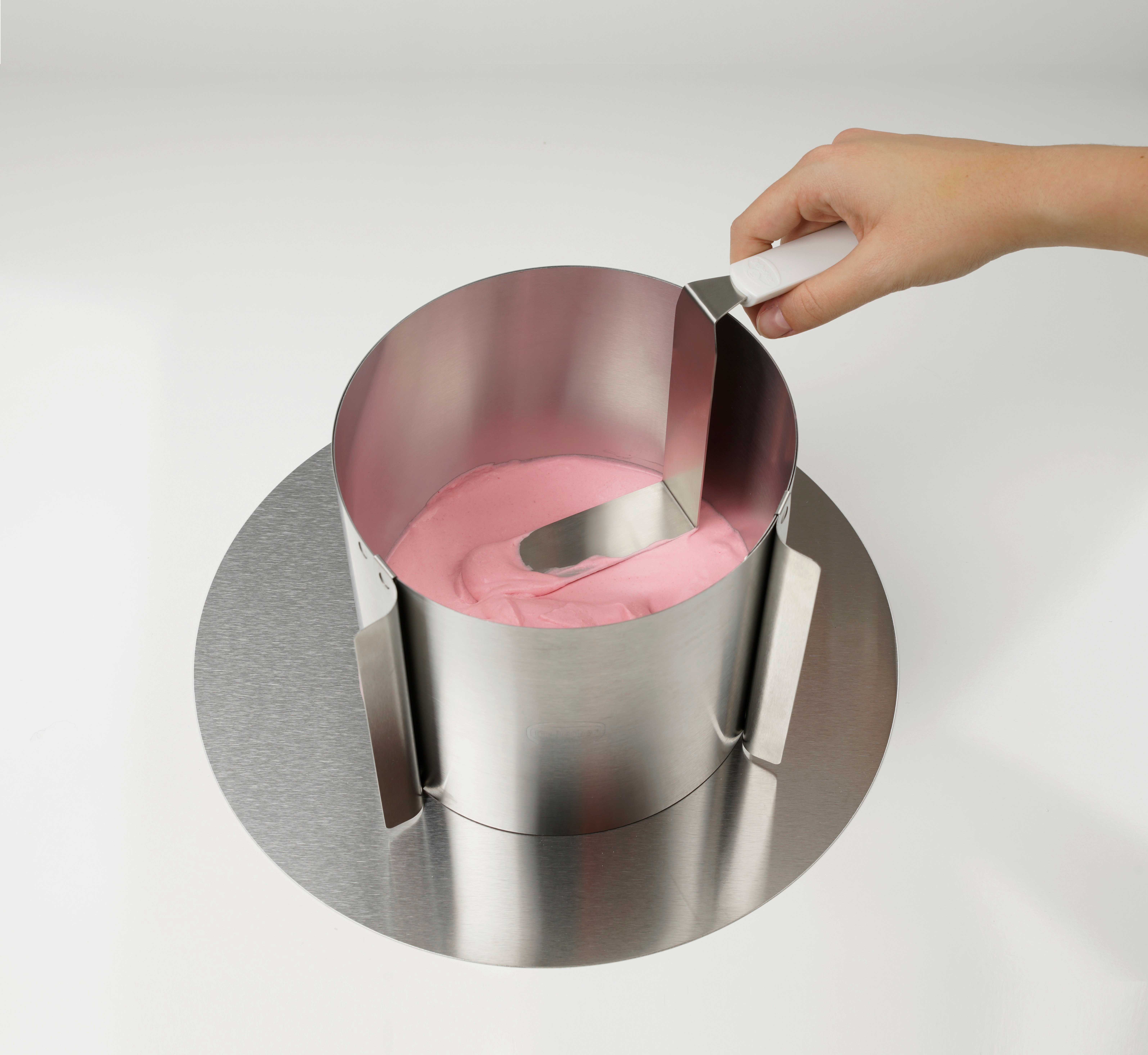 Eine Hand glättet mit einem Werkzeug rosa Teig in einem Kuchenring aus Metall.