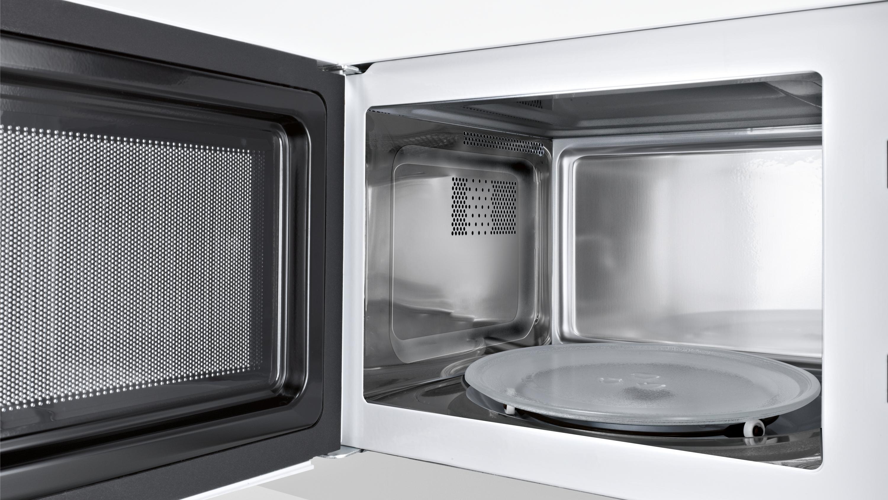 Dentro de un horno microondas. Plato de vidrio en el centro. Interior blanco, puerta abierta. Malla metálica.