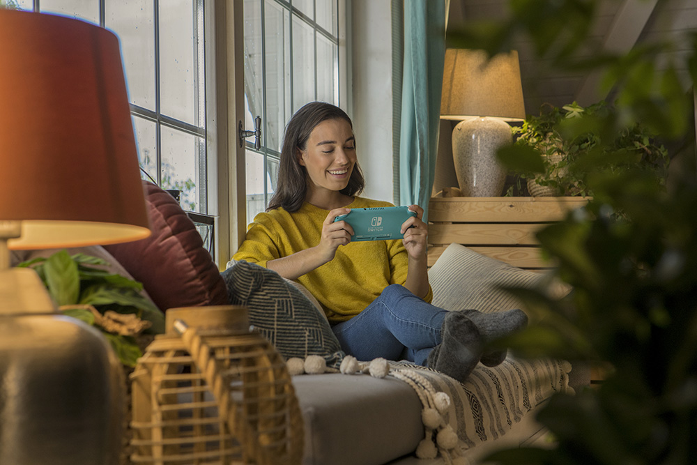 Vrouw op de bank speelt met een turquoise handheld gameconsole.
