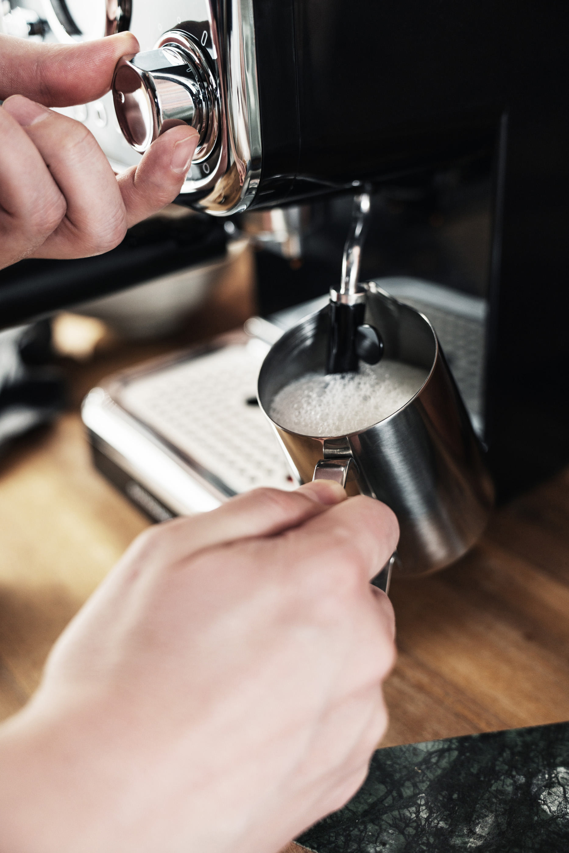 Hände gießen Milch in einen Metallkrug. Espressomaschine.