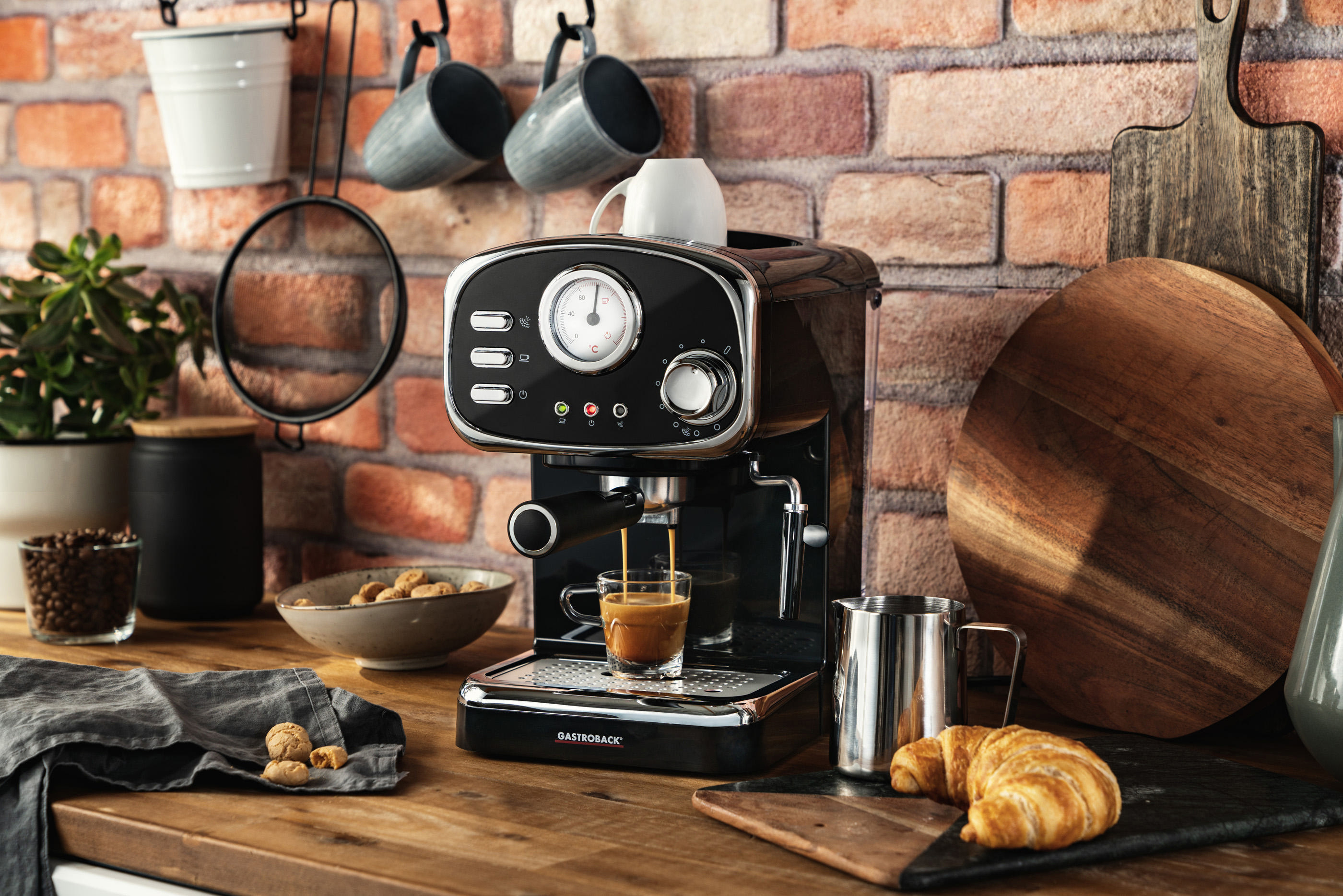 Eine schwarze Espressomaschine mit einem Glas Kaffee. Küchenumgebung mit Tassen, Brot und Deko.