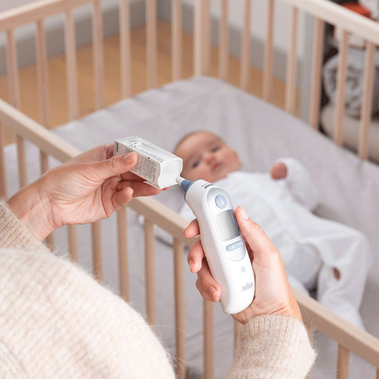 Persona che usa un termometro Braun su un bambino. Colori bianco e grigio.