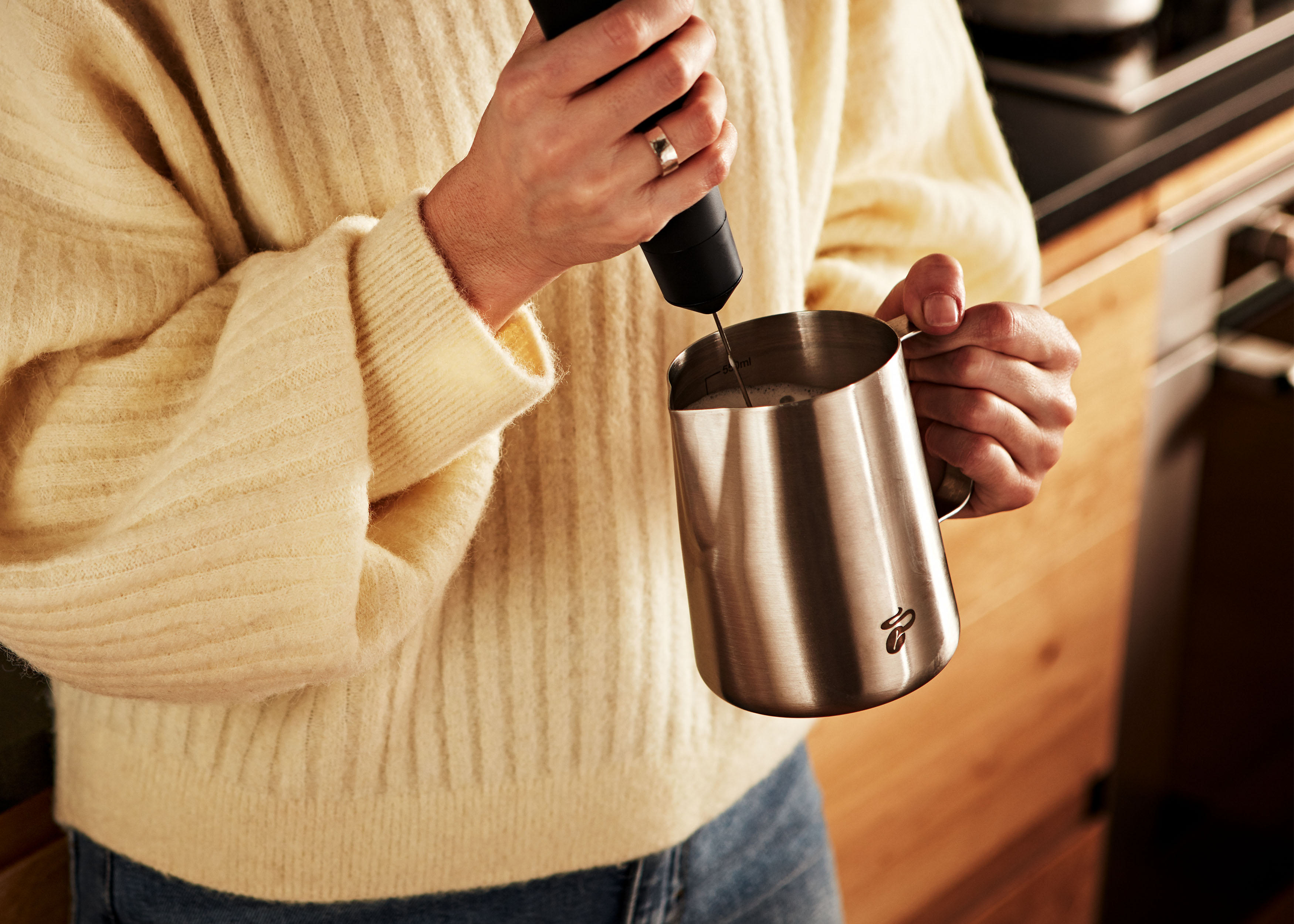 Eine Person verwendet einen Milchaufschäumer, um Milch in einem Metallkrug aufzuschäumen.
