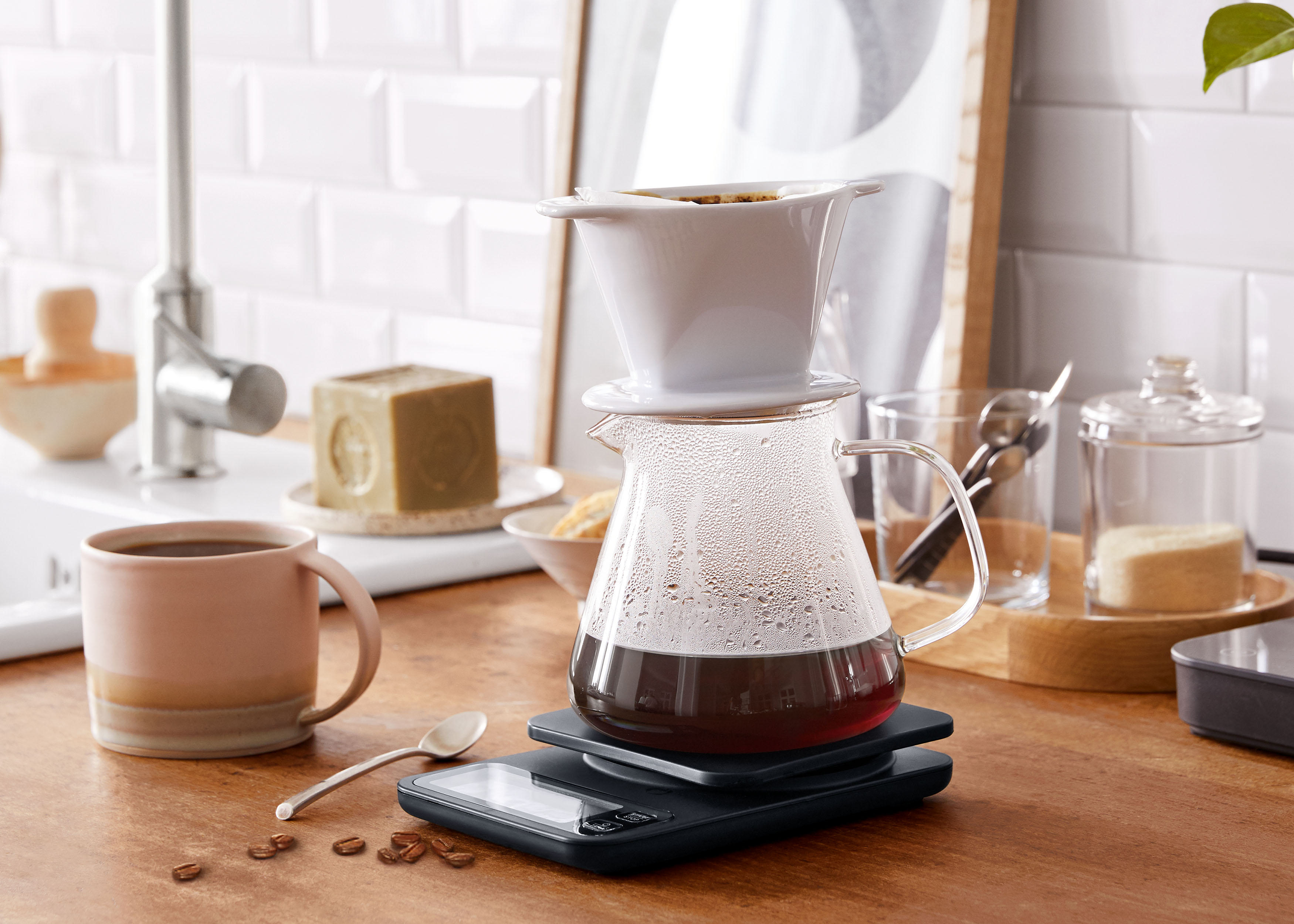 Kaffeezubereitung: Waage, Glaskaraffe, Filter und Tasse auf Holzküche.
