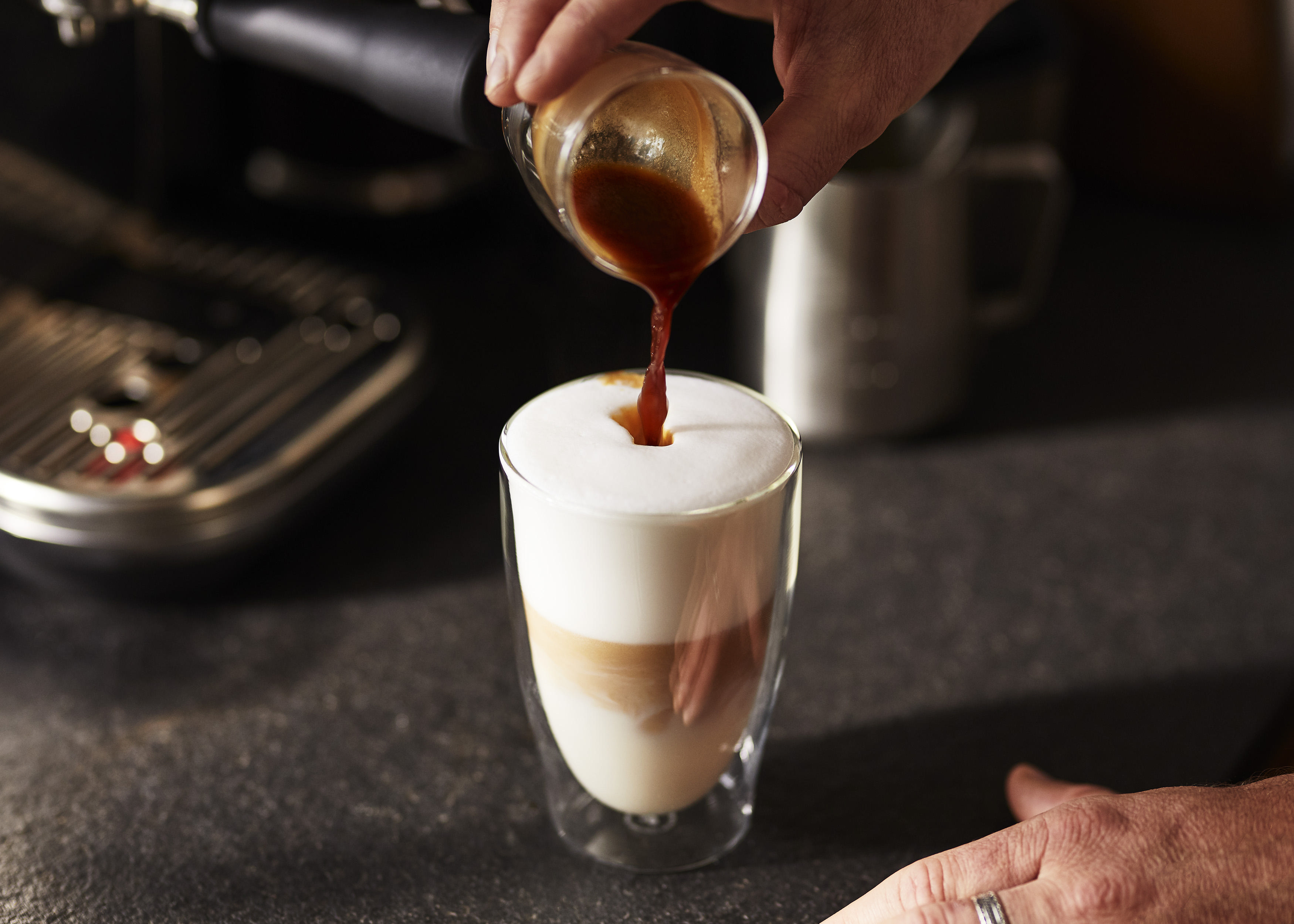 Espresso wird in ein Glas mit geschichtetem Latte gegossen, mit Hand.