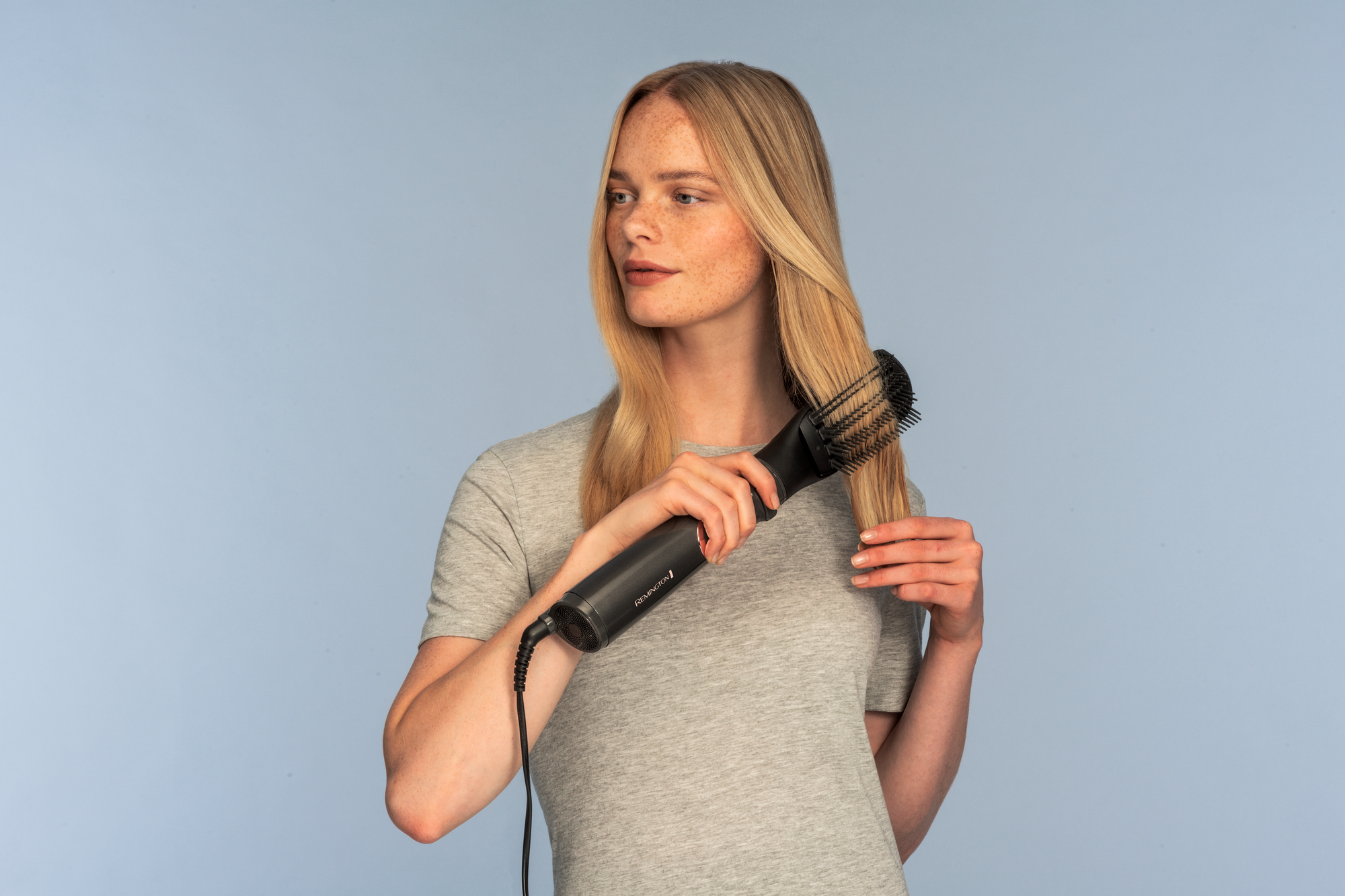 Eine Frau mit blonden Haaren benutzt eine schwarze Haartrocknerbürste für ihr Haar.