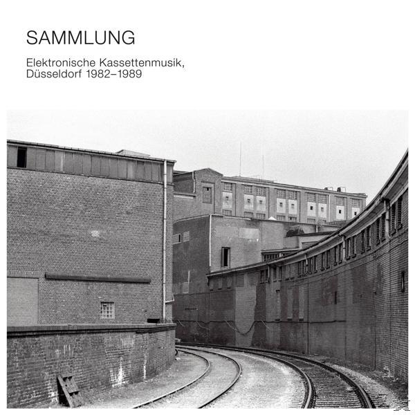 Schwarz-Weiß-Foto eines Gebäudes mit einer gekrümmten Bahntrasse davor.