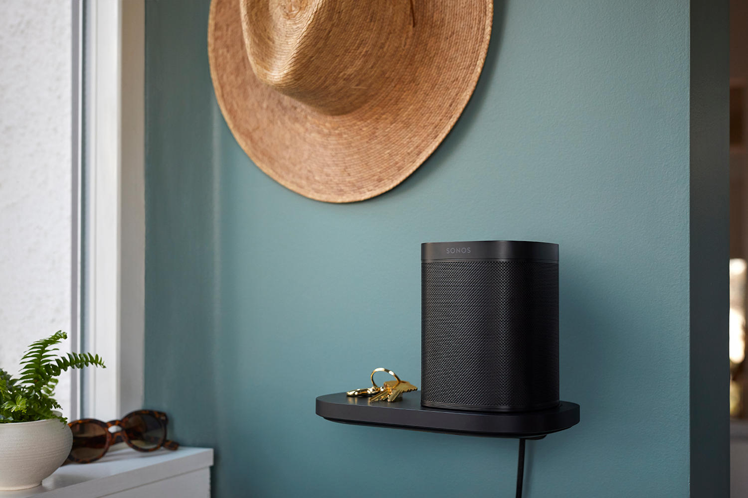 Black Sonos speaker on a shelf. A hat hangs above. Keys and sunglasses are on the shelf.
