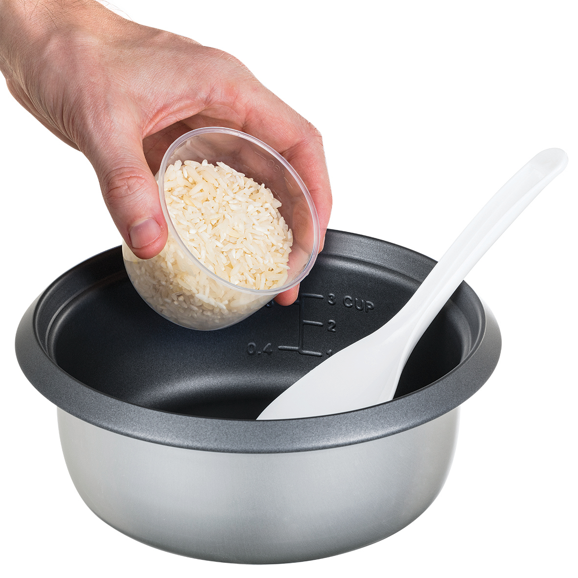Eine Hand gießt Reis aus einem durchsichtigen Becher in einen Reiskocher mit einem weißen Löffel darin.