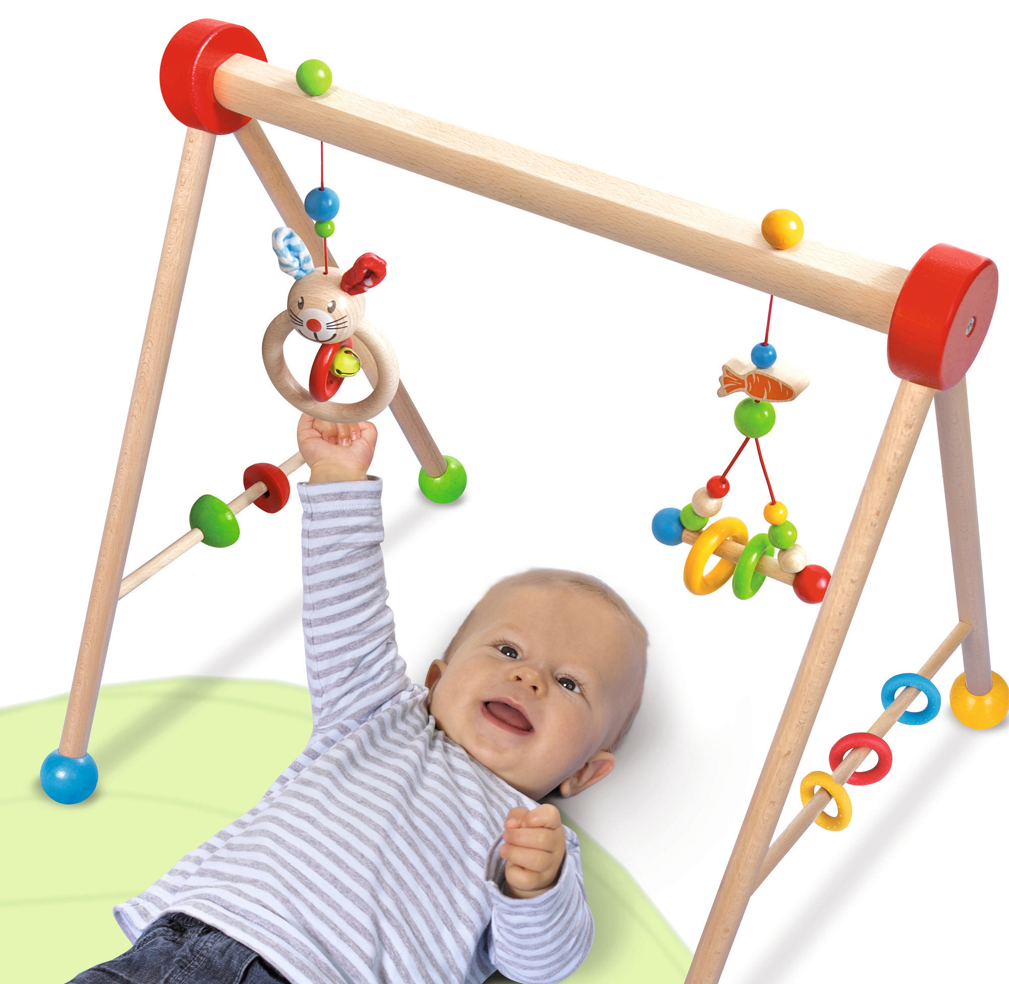 Ein Baby lächelt und greift nach Holzspielzeug für Babys. Das Fitnessstudio hat rote und grüne Akzente.