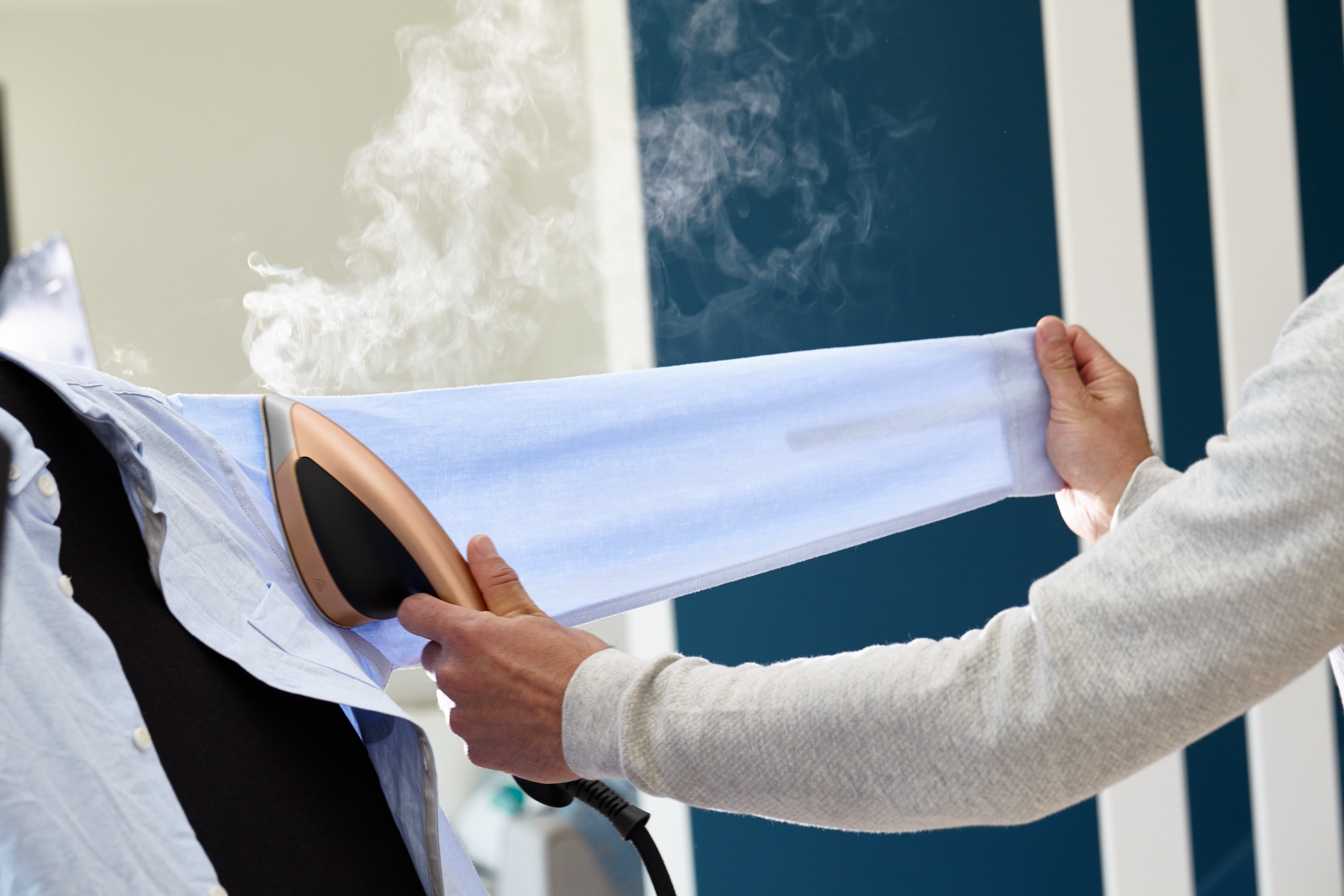 Eine Person bügelt ein blaues Hemd, hält den Ärmel mit einer Hand und das Bügeleisen mit der anderen.