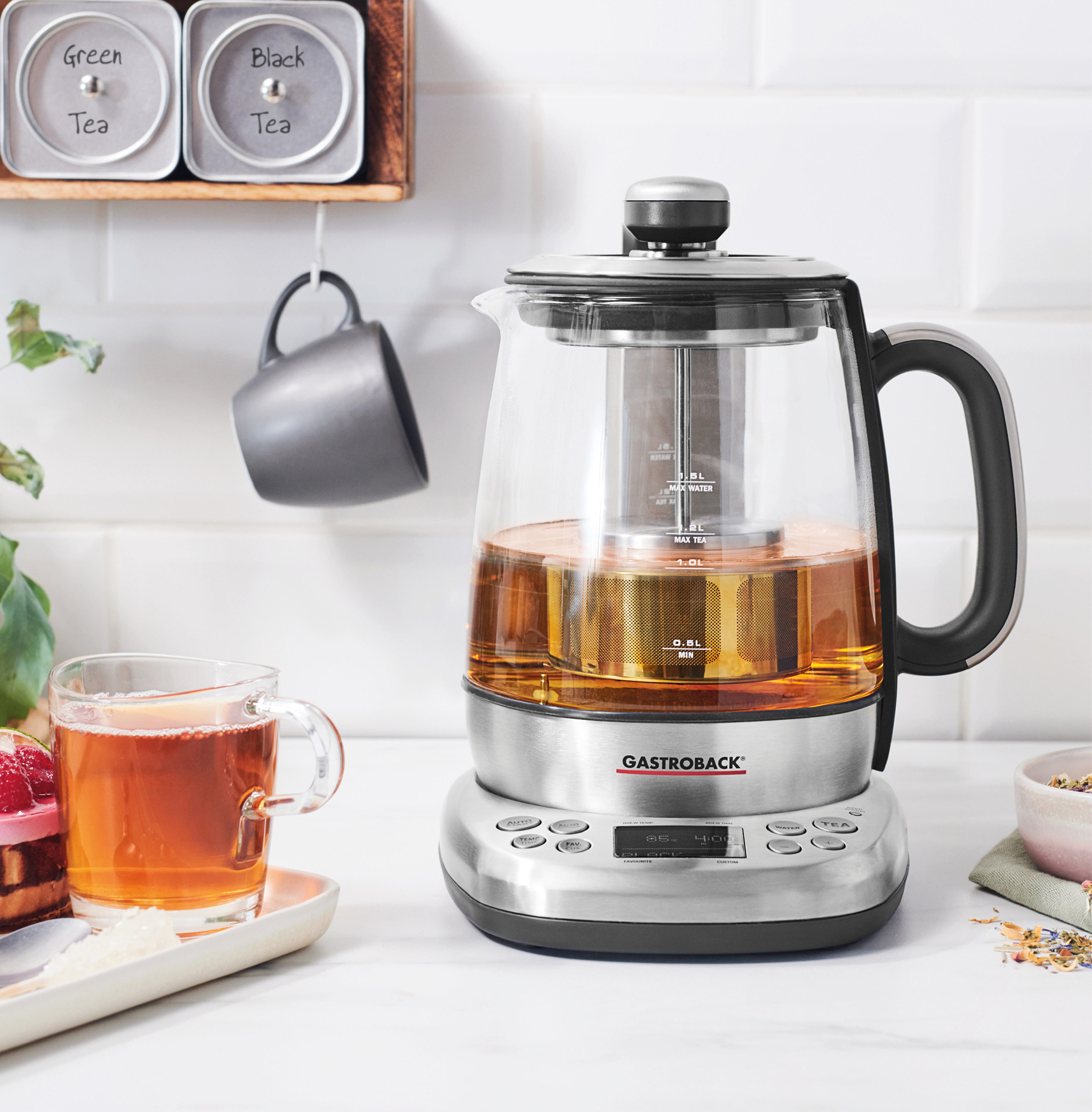 Gastroback Teezubereiter mit Tee, Tasse und Teezutaten auf weißer Oberfläche.