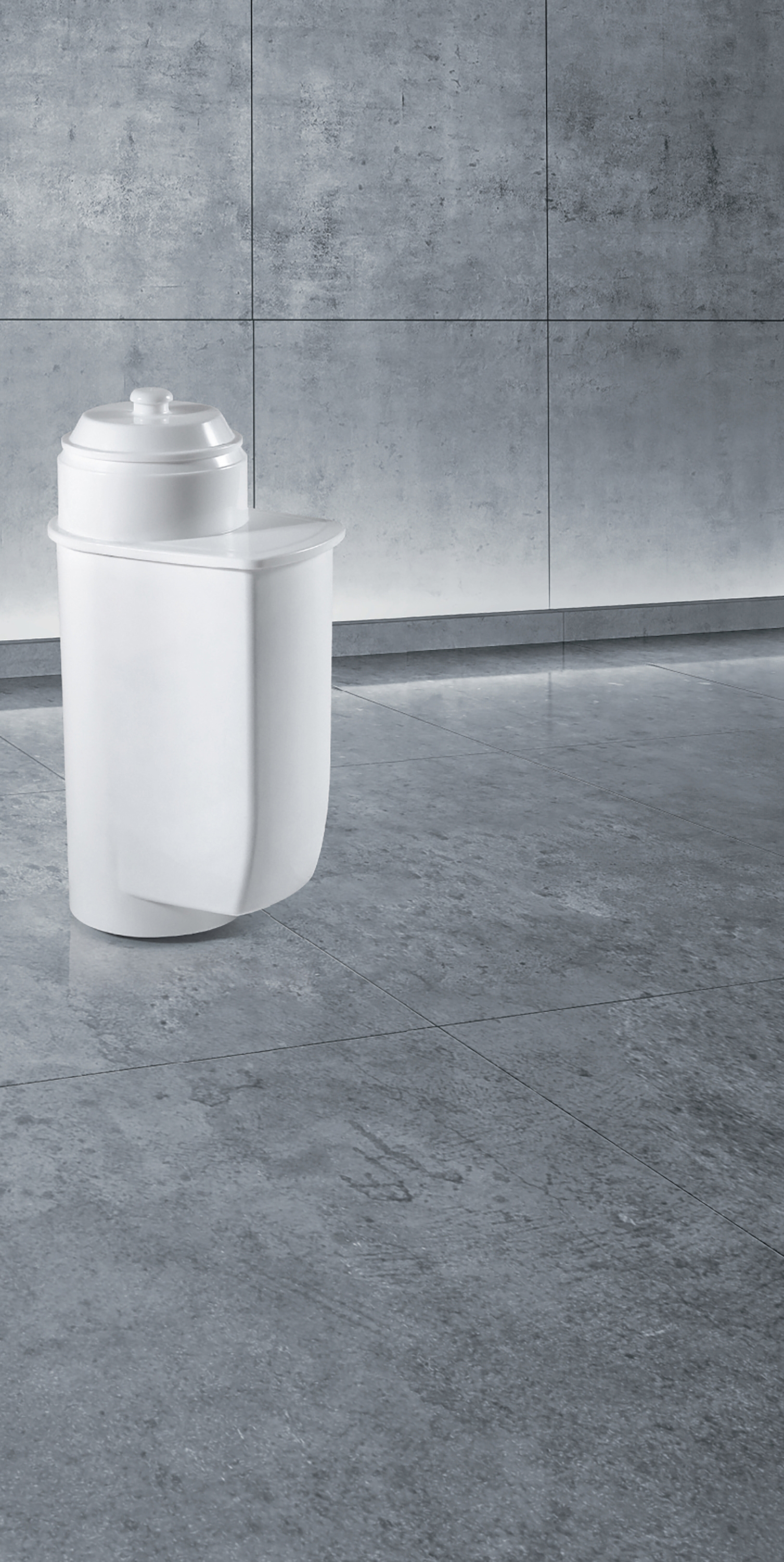 Weißer Wasserfilter auf grauem Boden. Graue Fliesenwand im Hintergrund.