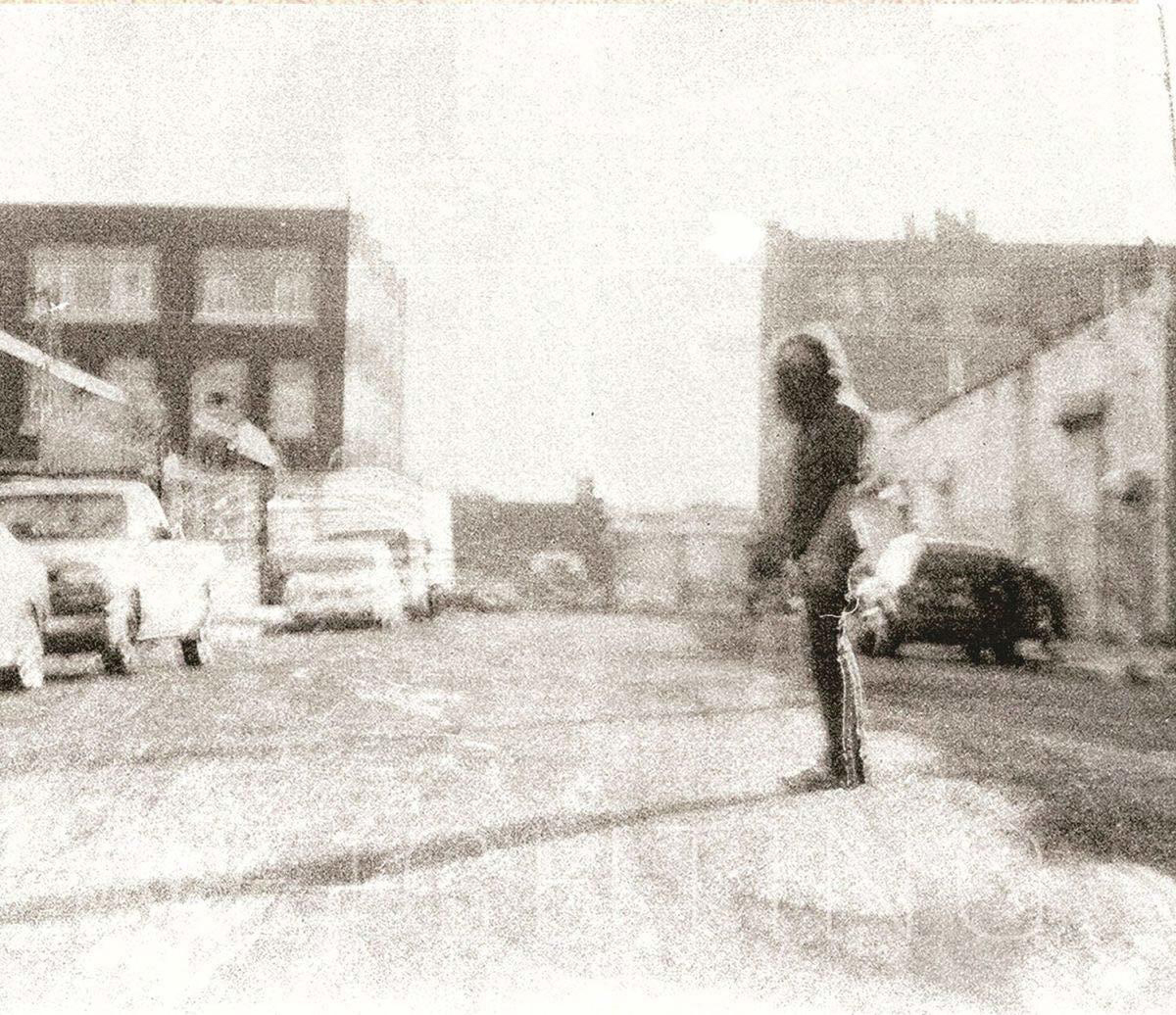 Schwarz-Weiß-Foto einer Straßenszene mit Autos. Eine Person steht in der Mitte.
