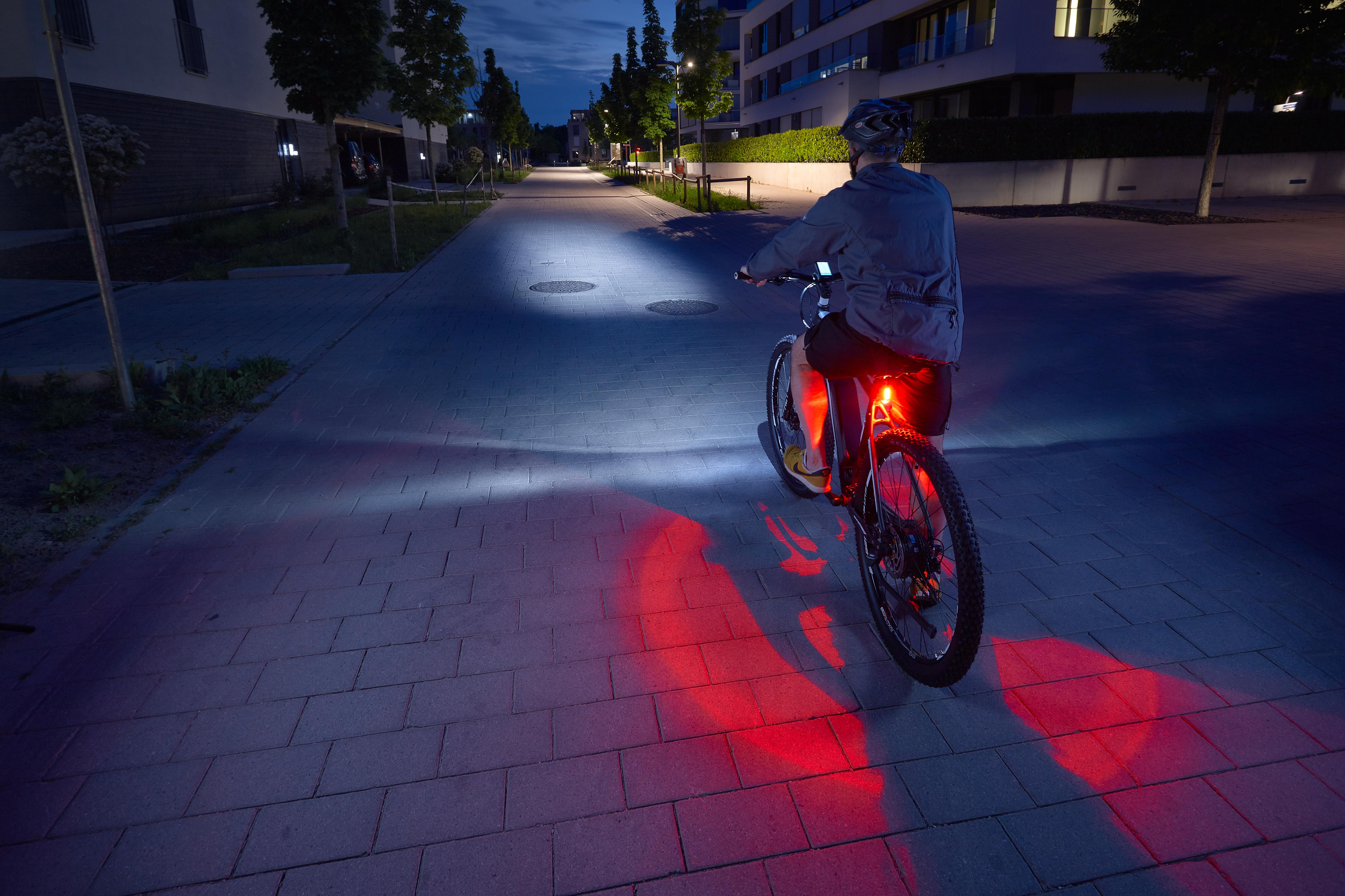 Person fährt nachts mit eingeschaltetem Licht Fahrrad auf einer Ziegelstraße.