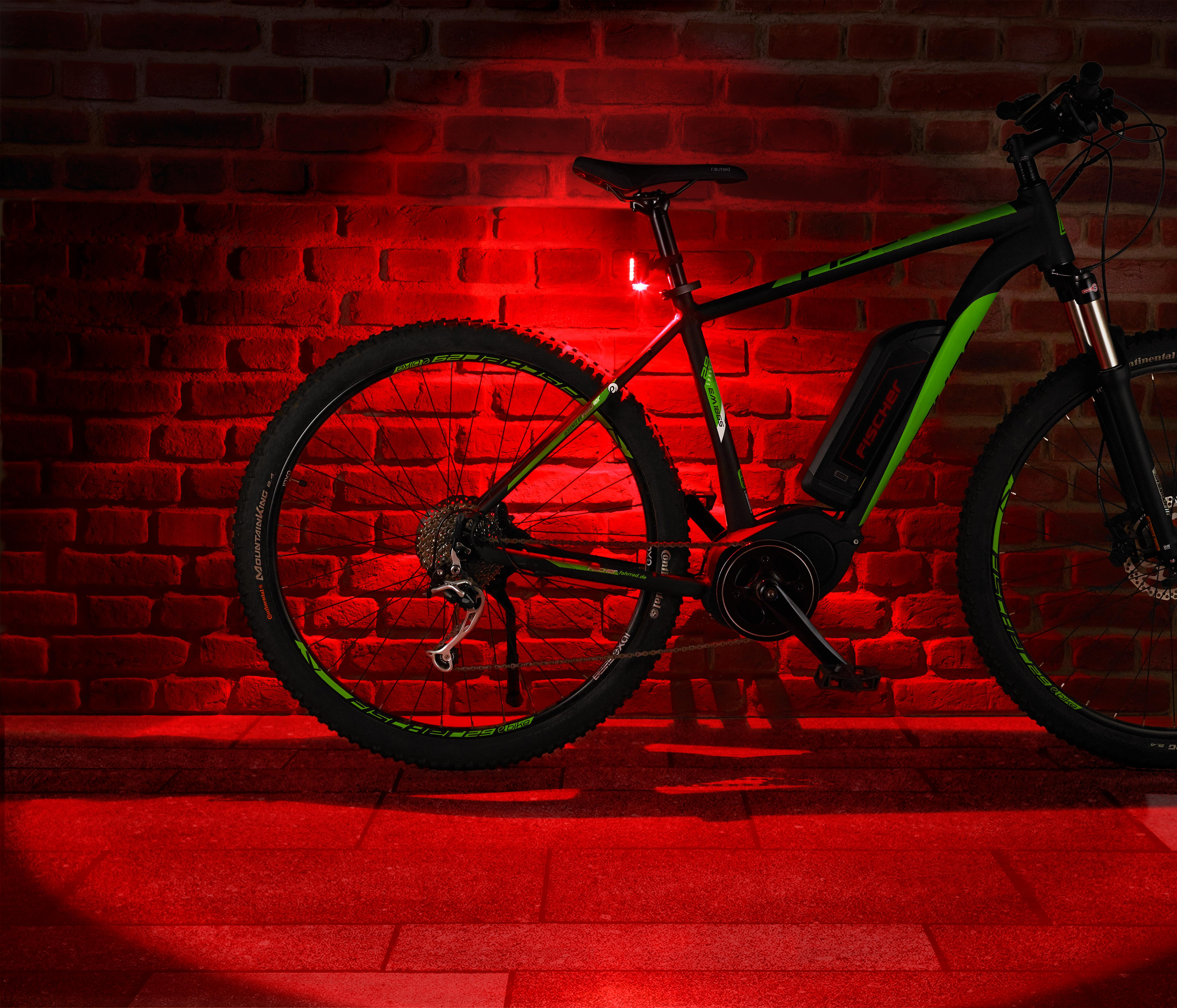 Ein schwarz-grünes Elektrofahrrad, das mit rotem Licht beleuchtet wird. Rote Backsteinmauer im Hintergrund.